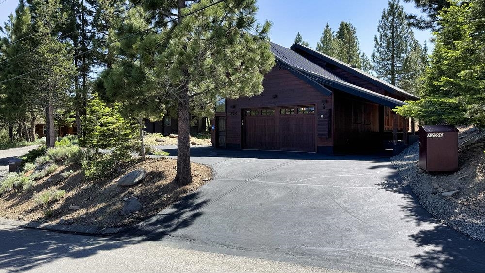 Wooded home with a wide driveway and dark wood garage.