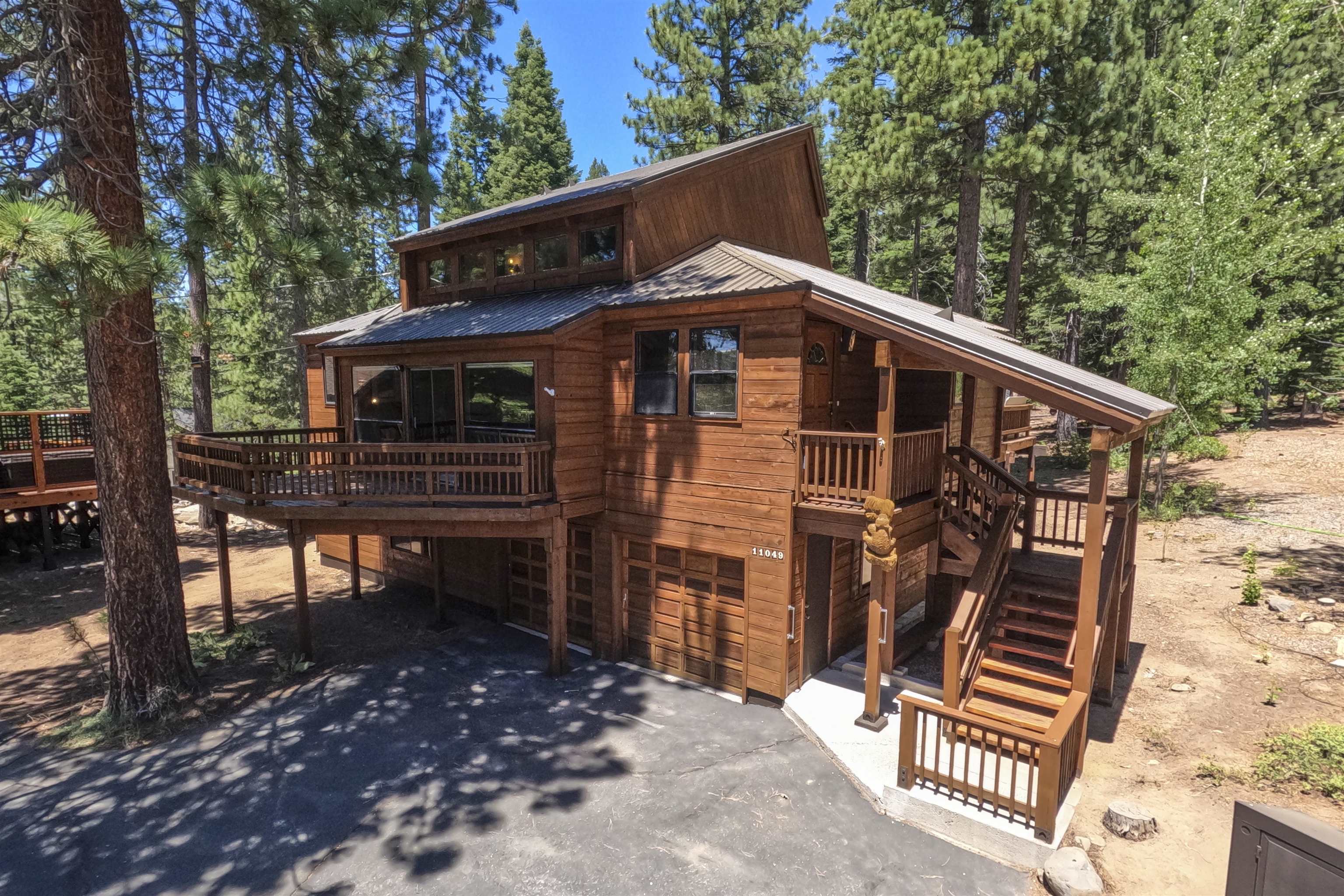 Multi-level wood cabin with wraparound decks and exterior stairs among pine trees.