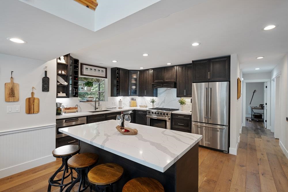 Remodeled kitchen with a white island, dark cabinets, stainless steel appliances, and wood floors.