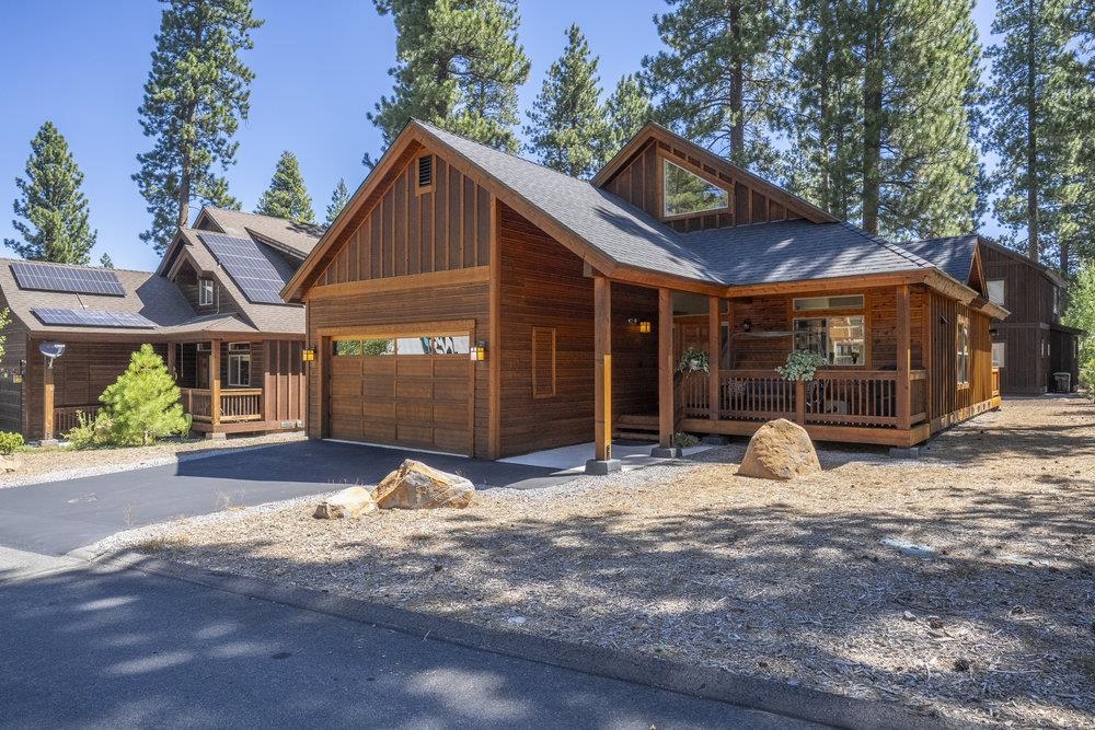 Timber house with a two-car garage and covered porch among pine trees.