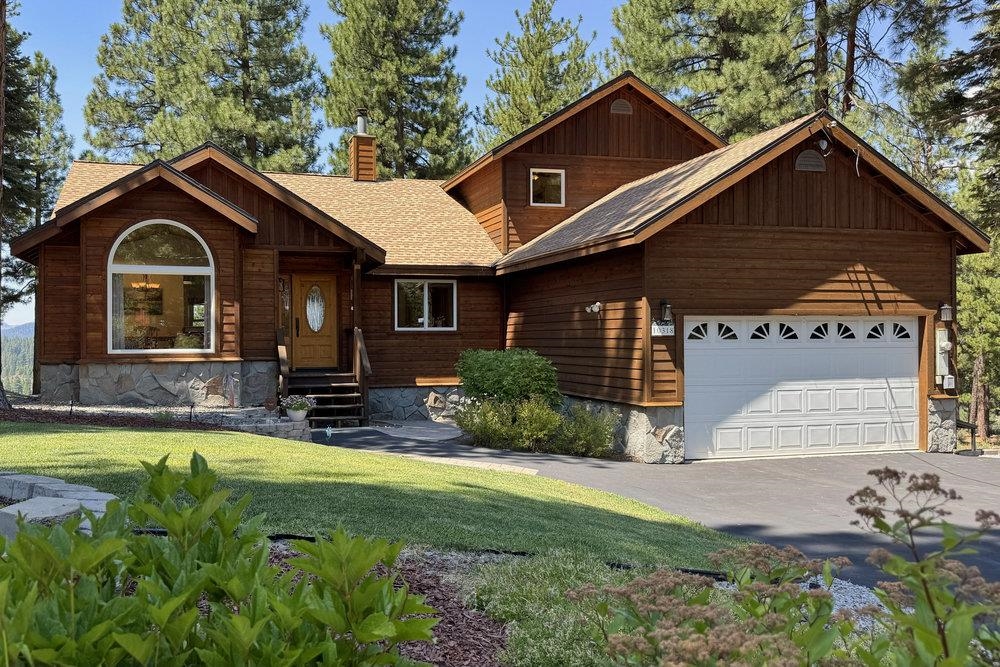 Wood-sided house with an arched front window, stone foundation, and attached garage among pine trees.