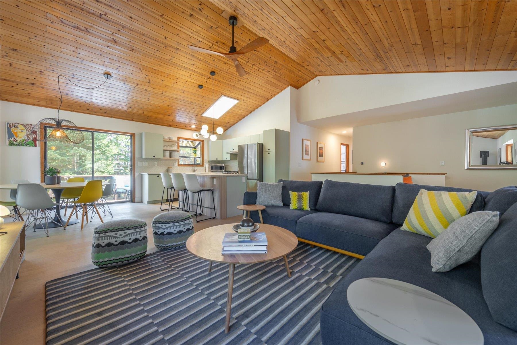 Open-plan living room with a blue sectional beneath a vaulted wood-plank ceiling.
