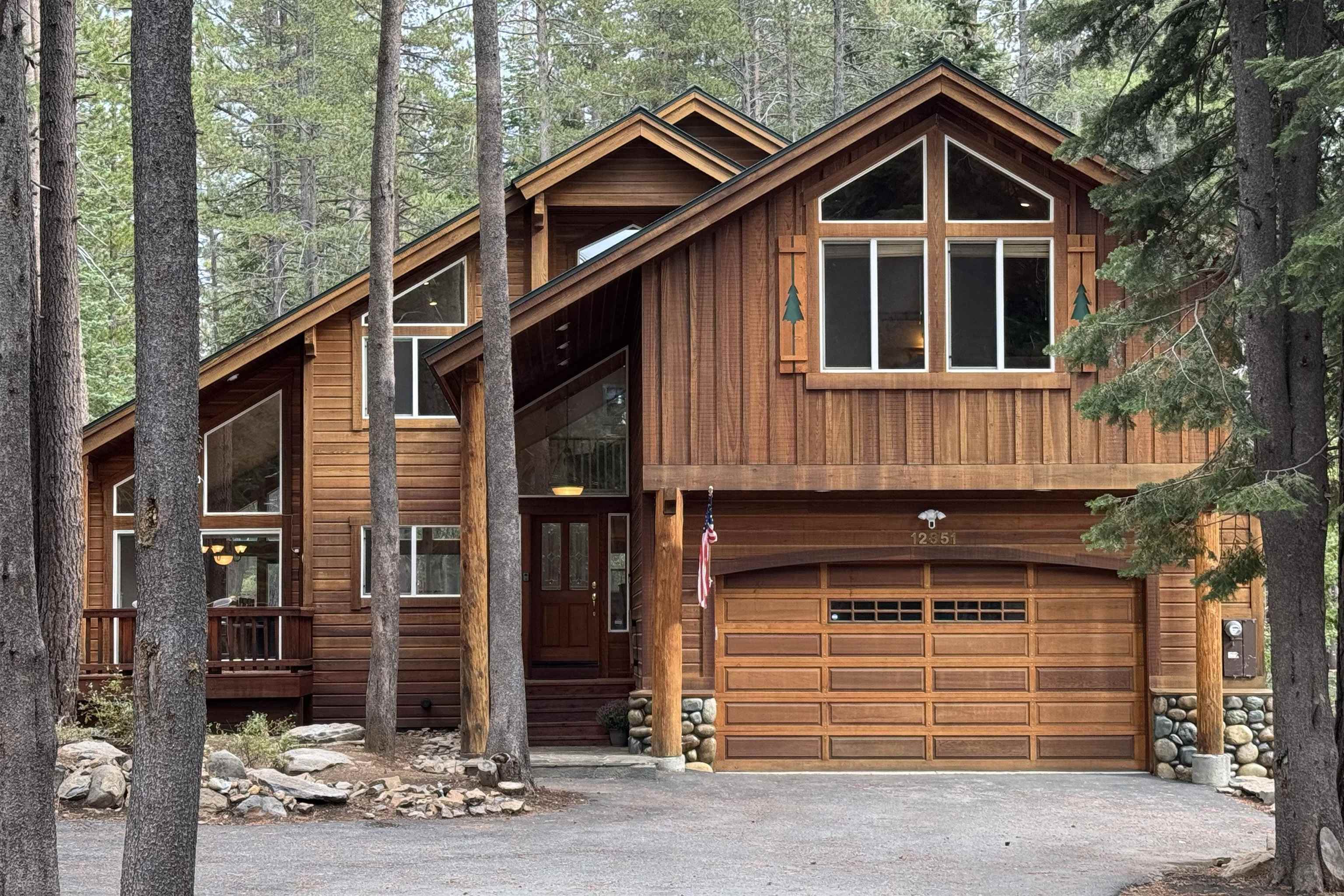Wood-sided home with multiple gables and a large garage, nestled among tall pine trees.