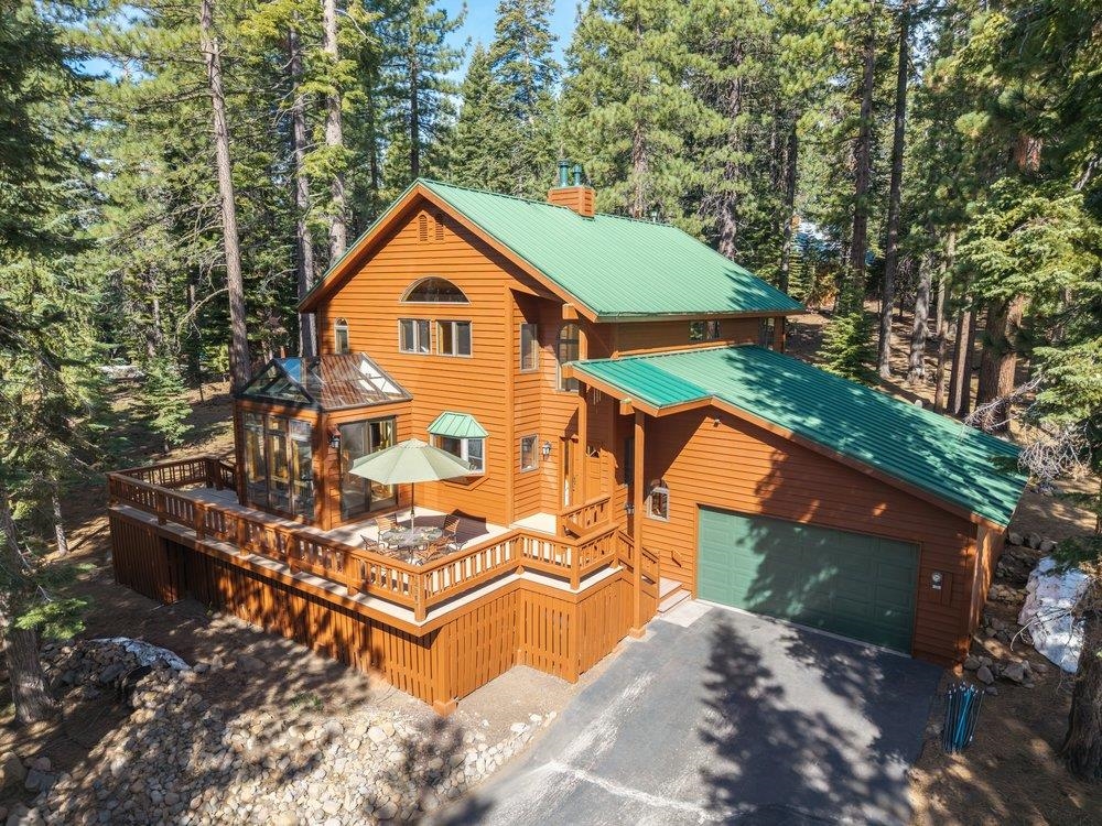 Orange wood home with green roofs and a wraparound deck among tall evergreen trees.