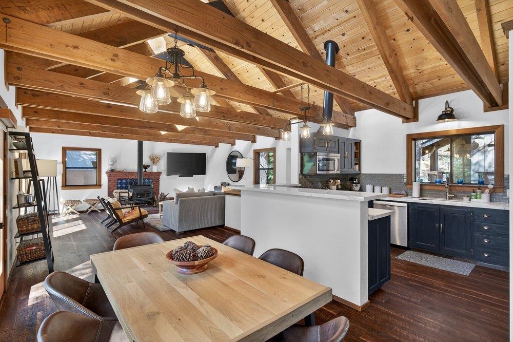 Open-plan kitchen and living area with a large island, brick fireplace, and exposed timber beams.