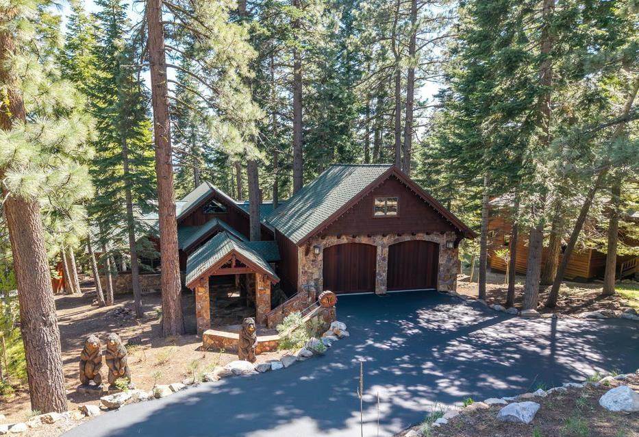 Rustic wood-and-stone house with a two-car garage nestled among tall pine trees.