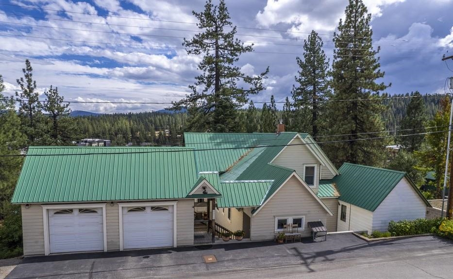 Home with green metal roofs and a two-car garage, backed by pine trees and forested hills.