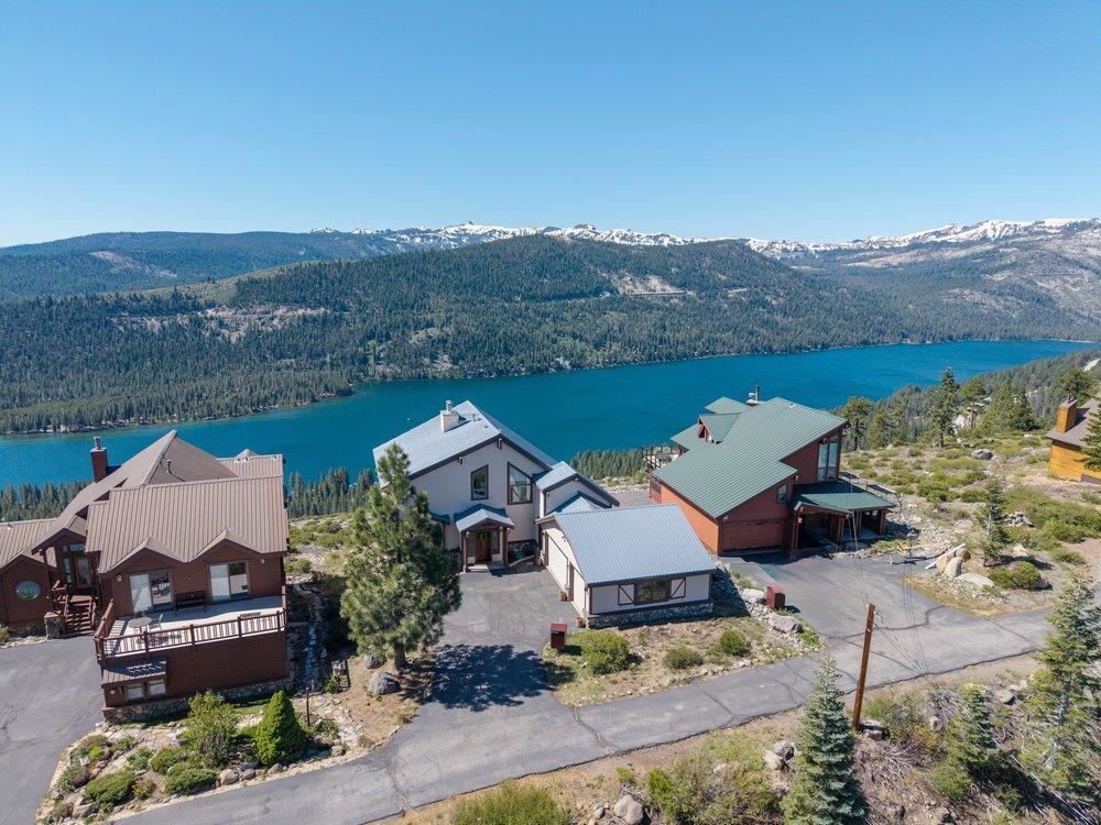 Hillside homes overlook a blue lake and forested, snow-dusted mountains.