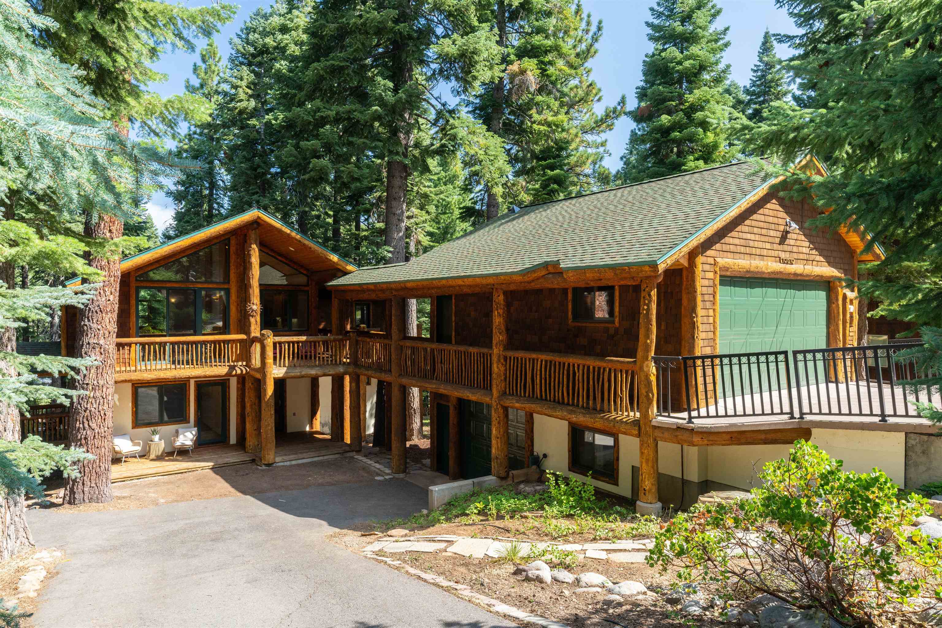Woodland home with timber balconies, a green garage door, and tall evergreens surrounding it.