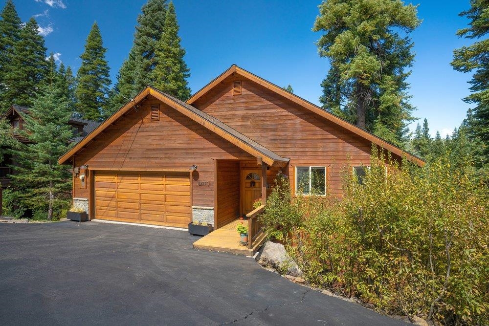 Wood-sided home with a two-car garage and covered entry among tall evergreen trees.