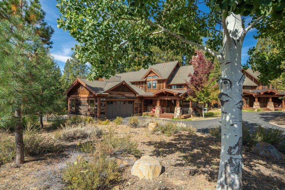 Rustic timber house with a two-car garage and covered porch among mature trees.