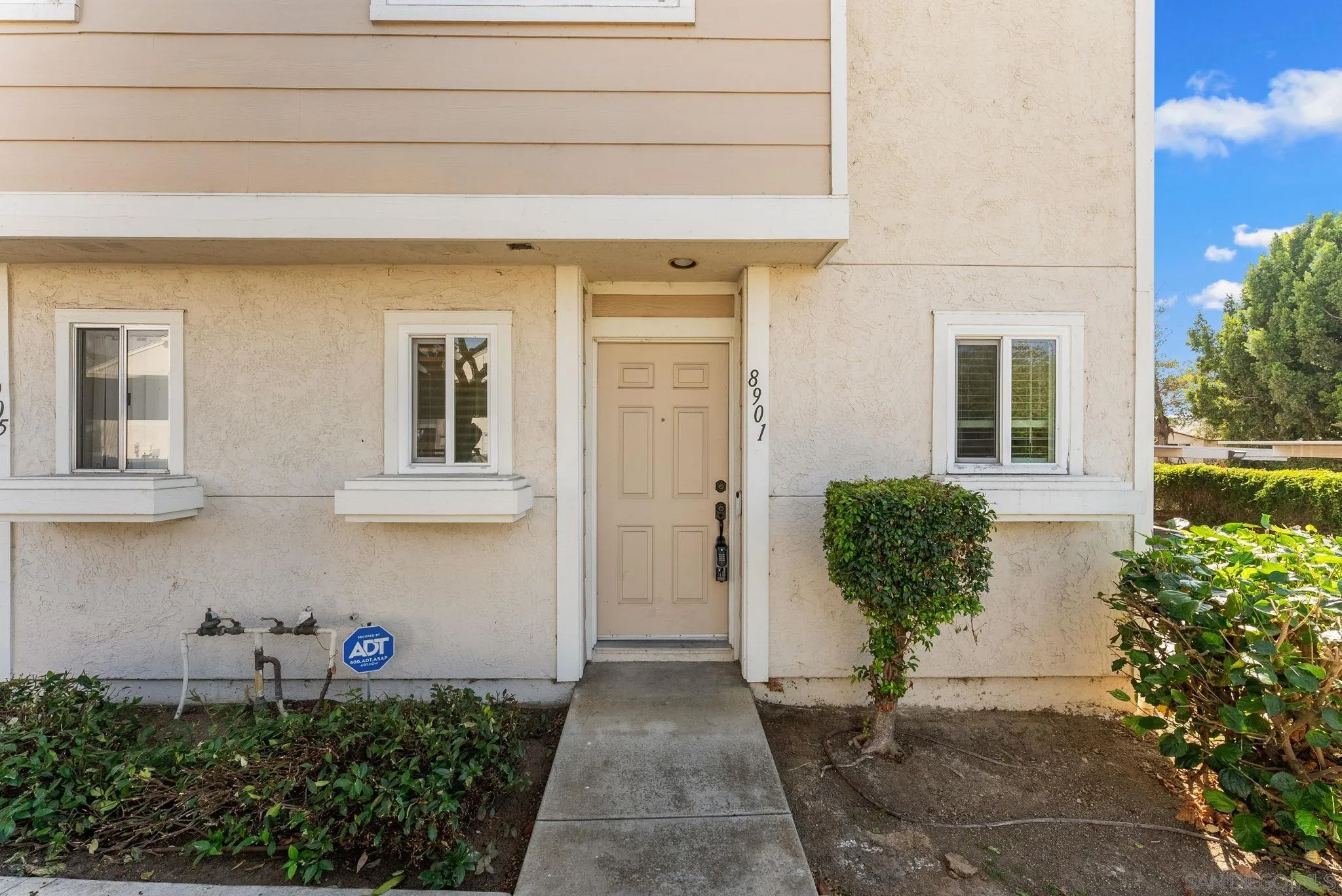 Home entrance with beige paneled door, white-trimmed windows, and a concrete walkway.