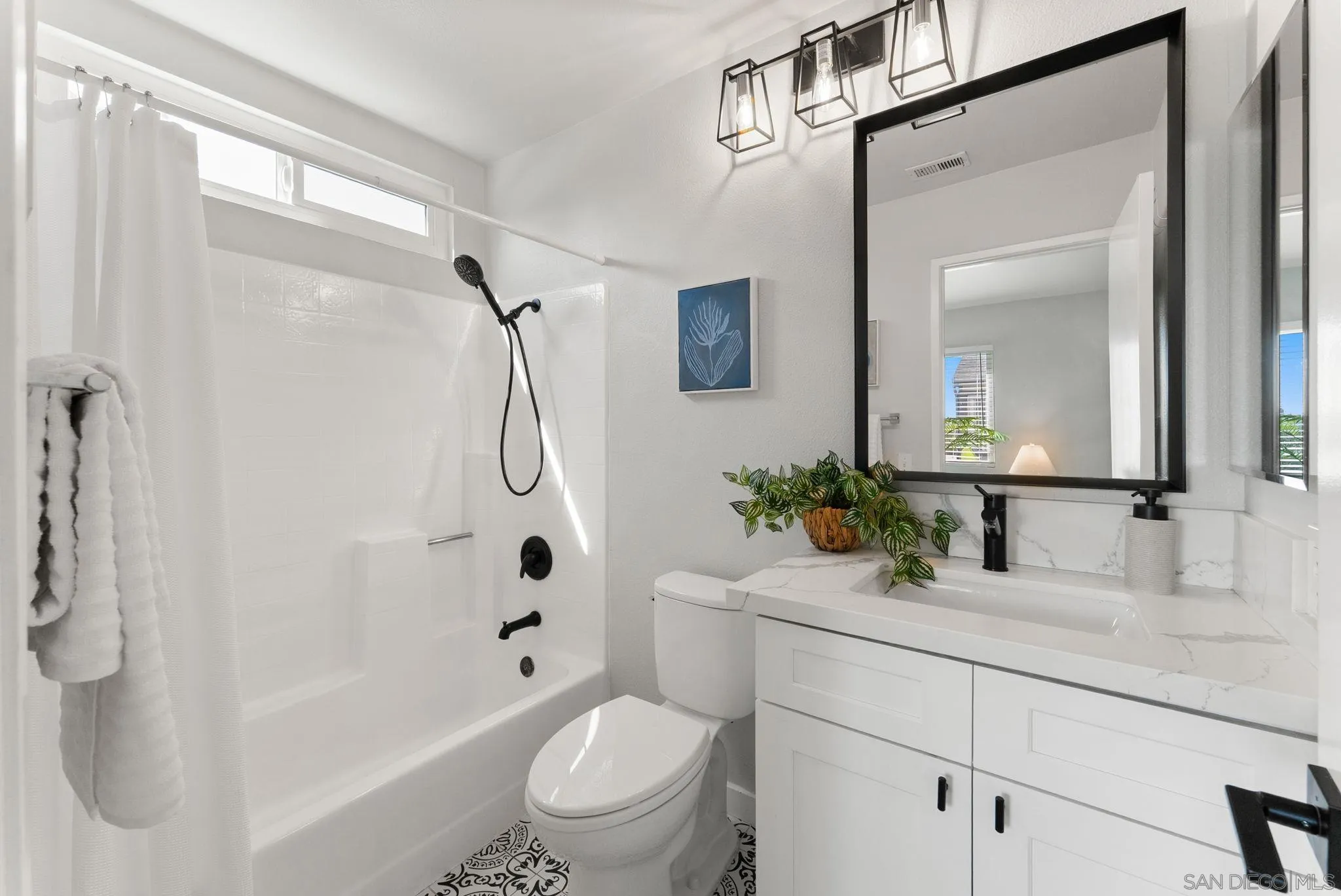 Bright bathroom with a white tub, black shower fixtures, patterned tile, and a white vanity.