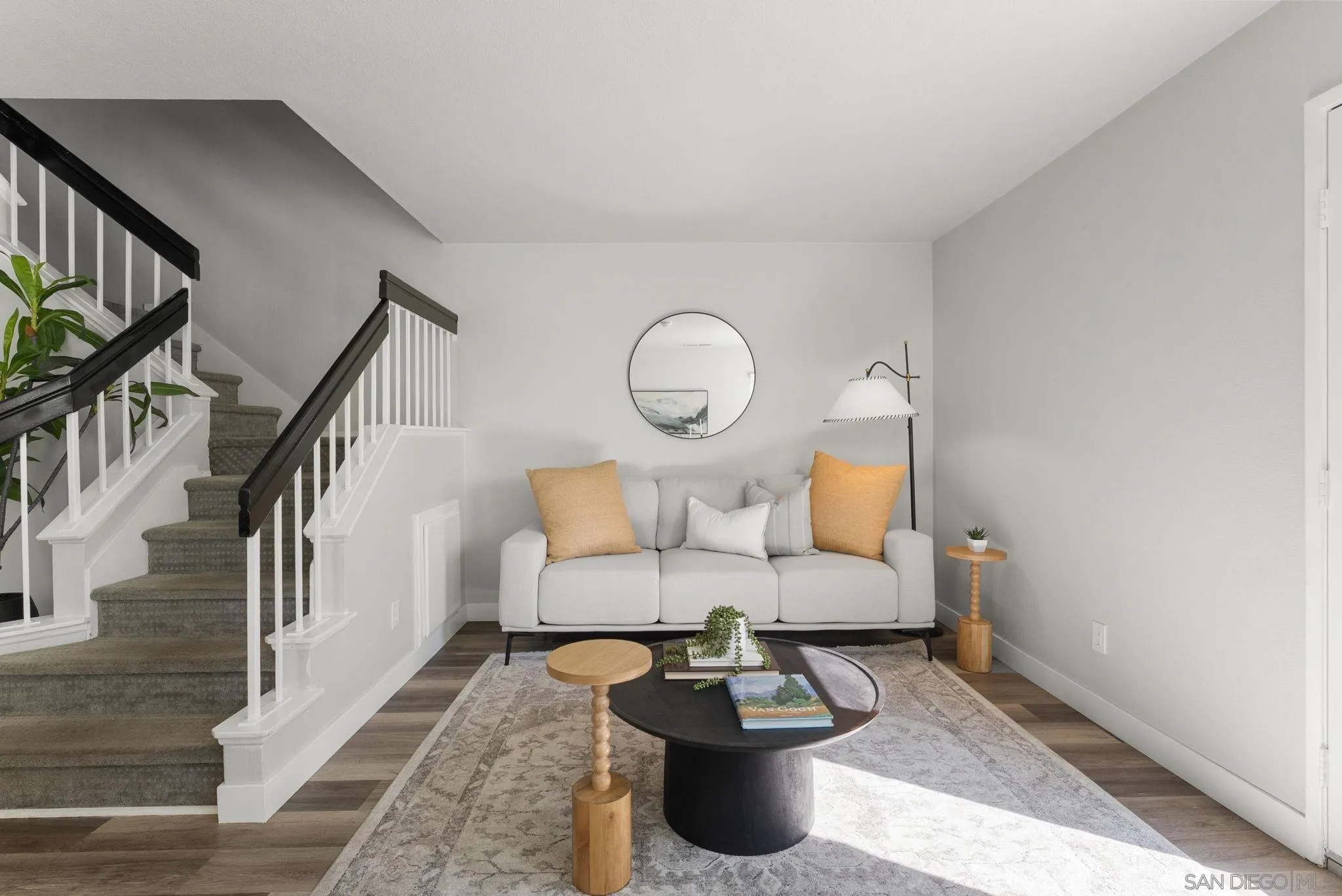 Furnished living room with a gray sofa, mustard cushions, and a staircase with dark handrails.
