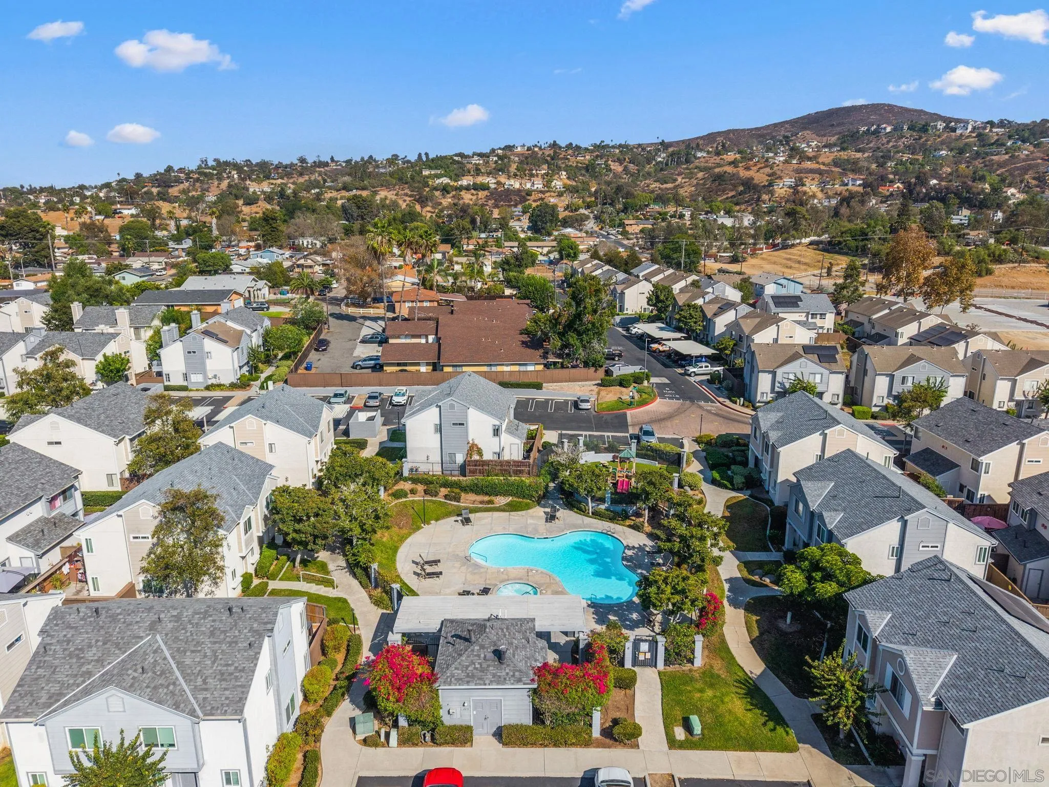 Aerial view of a residential community with a central swimming pool and hills in the distance.
