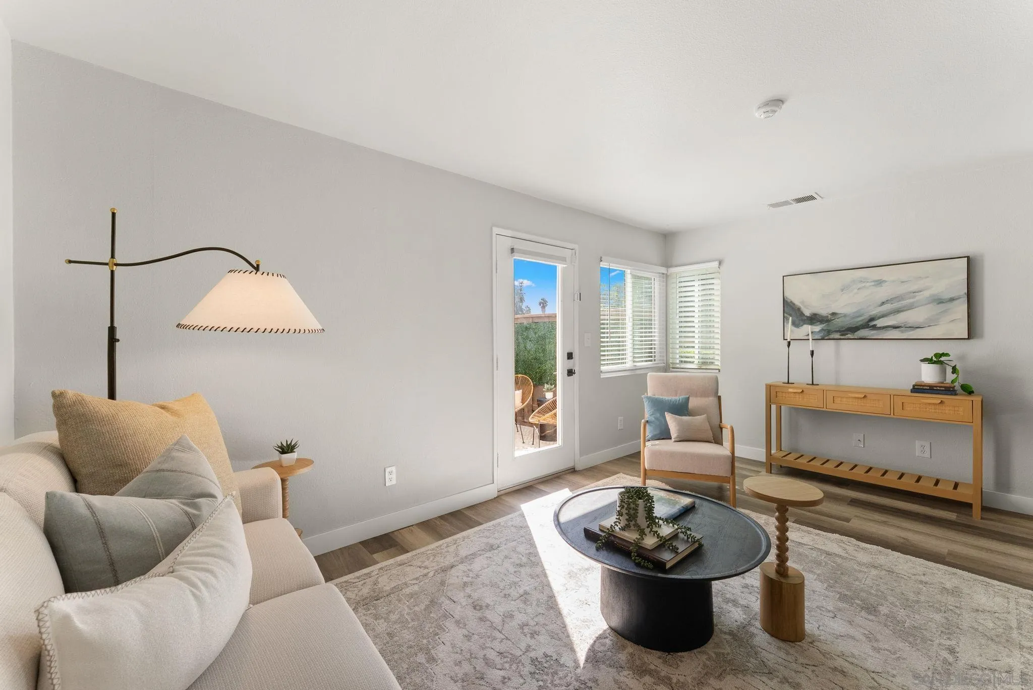 Staged living room with a cream sofa, armchair, round coffee tables, and a glass door opening to a patio.
