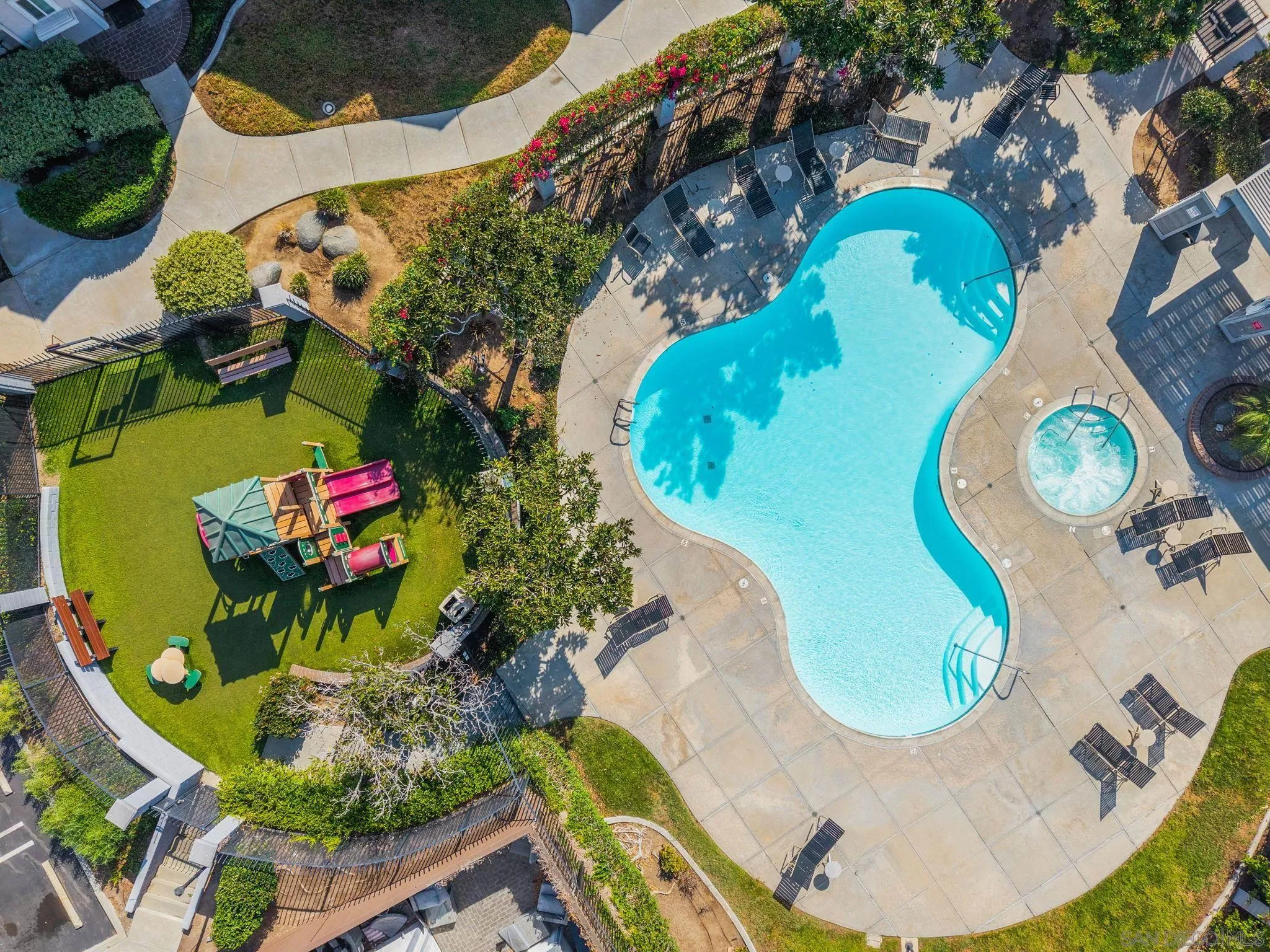 Aerial view of a curving community pool and spa beside a fenced playground.