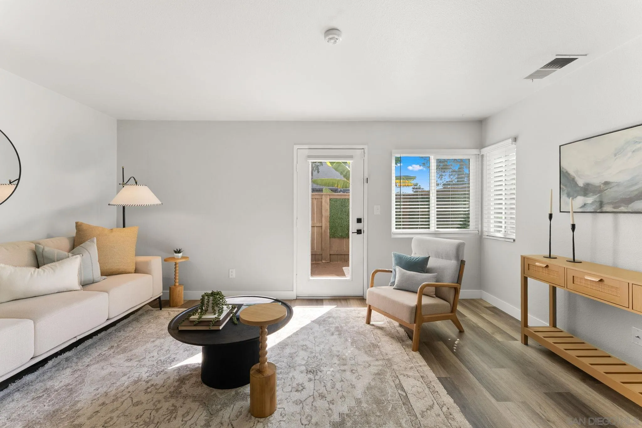 Staged living room with a light sofa, accent chair, and shuttered windows beside a glass-paneled door.