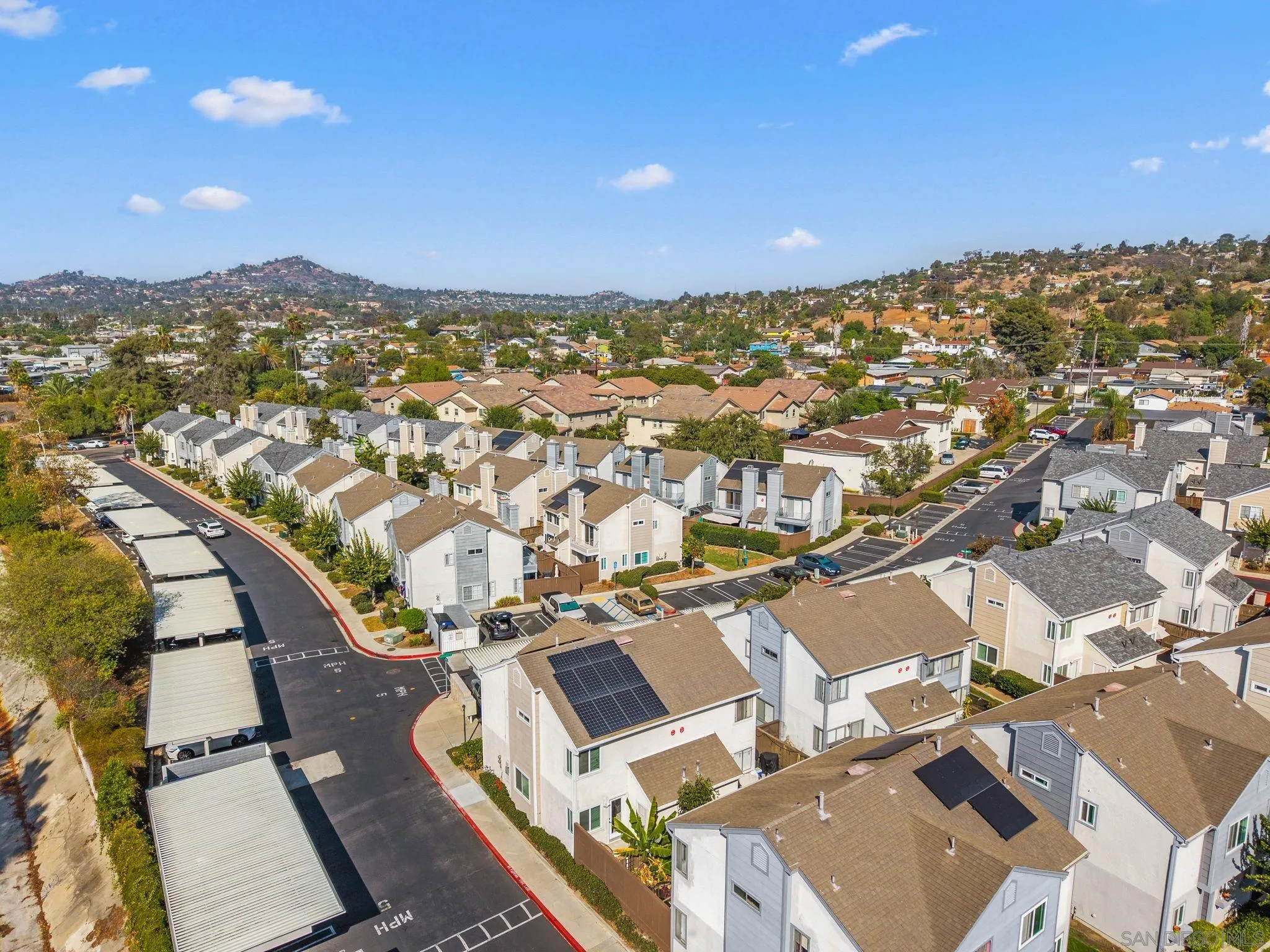 Aerial view of a townhome neighborhood with carports, rooftop solar panels, and rolling hills beyond.