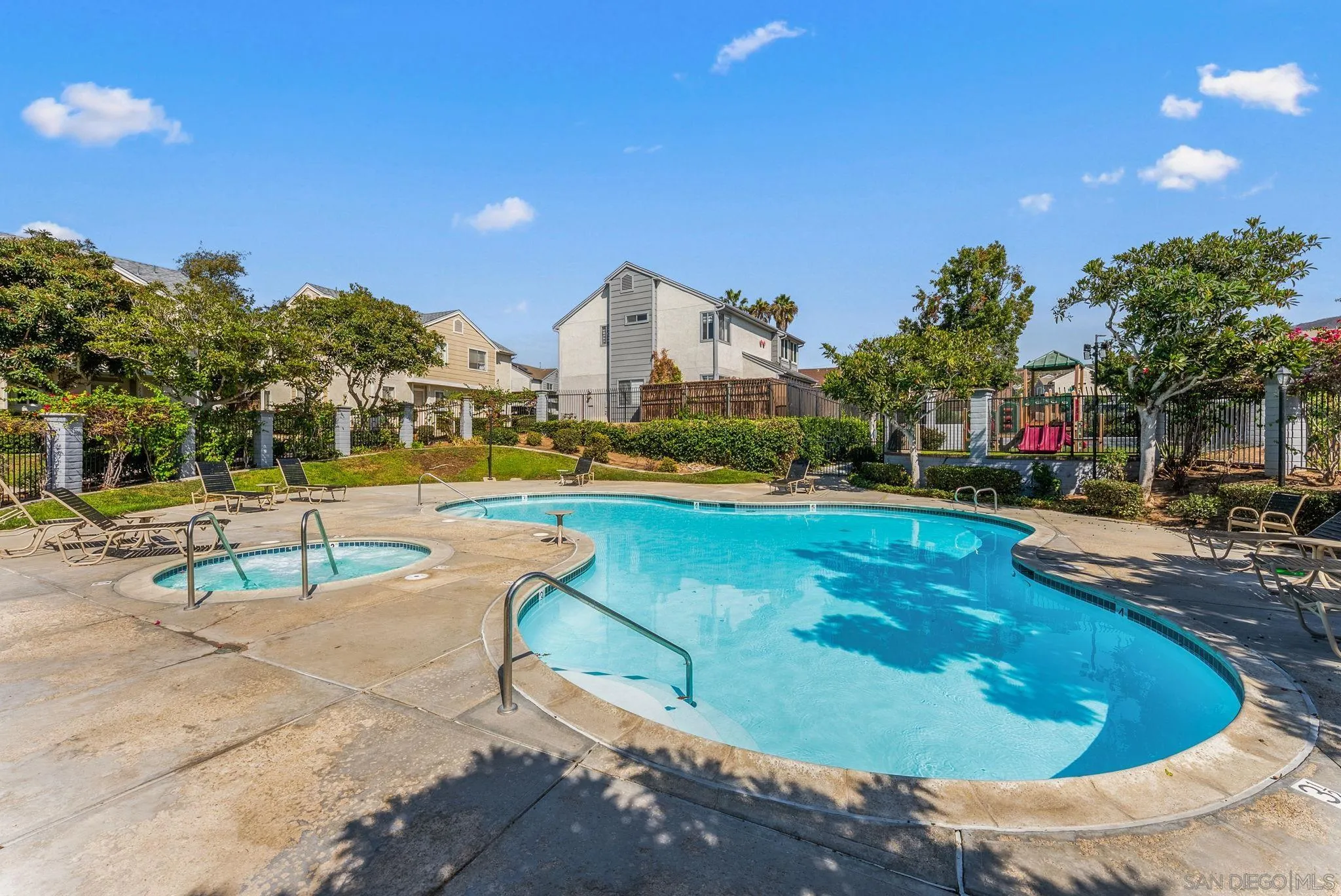 Community swimming pool and attached spa with lounge chairs, landscaped trees, and nearby homes.