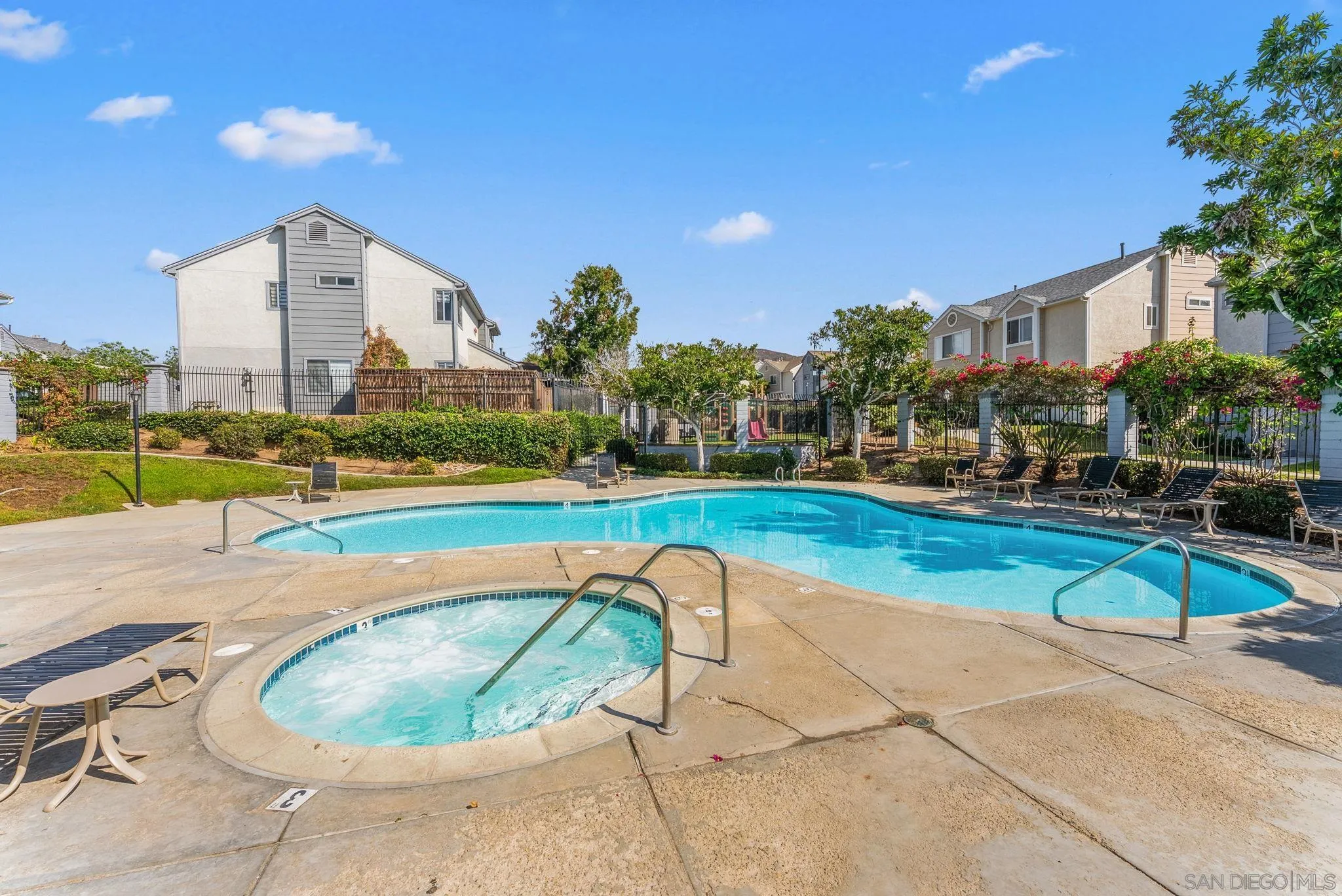 Community pool and bubbling spa with lounge chairs and residences nearby.