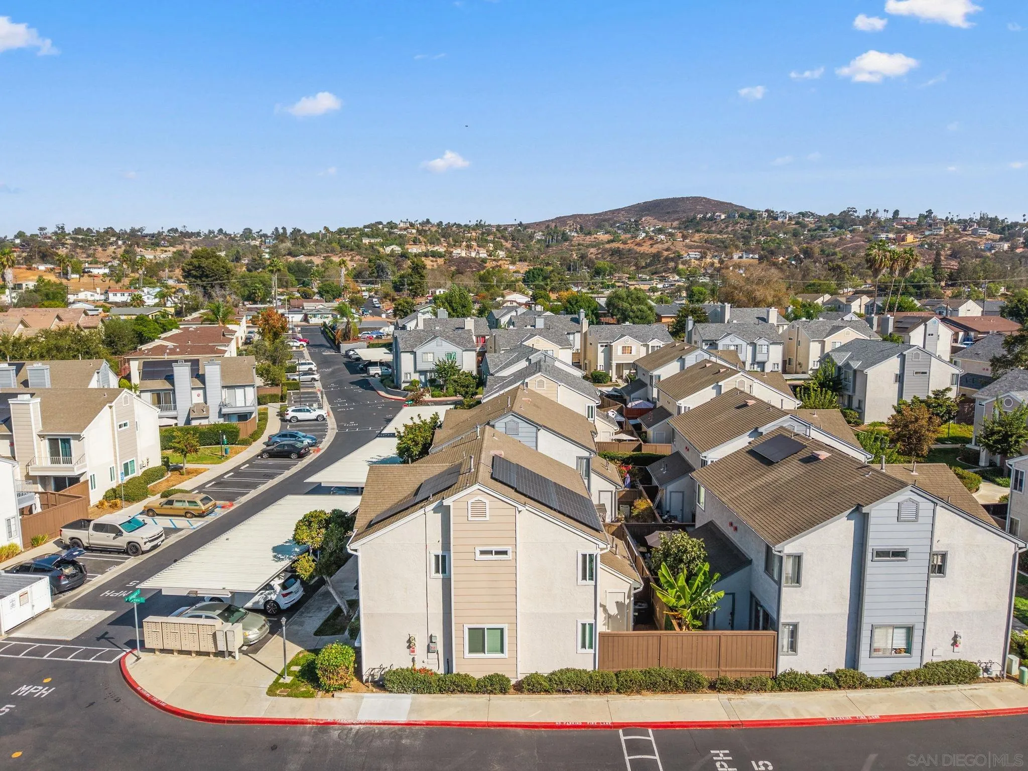 Aerial view of attached homes with rooftop solar panels, parking, and dry hills in the distance.