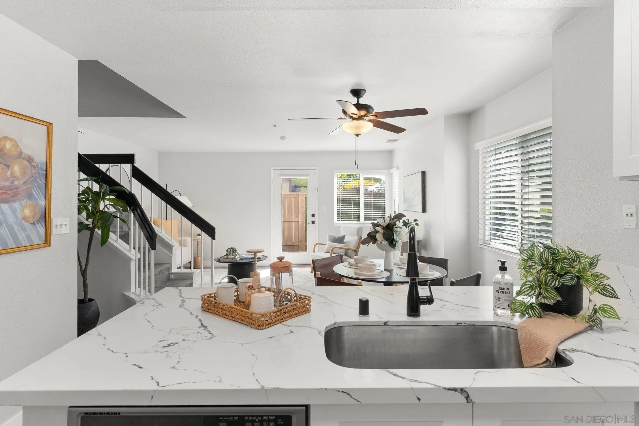 Open-plan kitchen with a marble-veined island, black faucet, dining area, and staircase.
