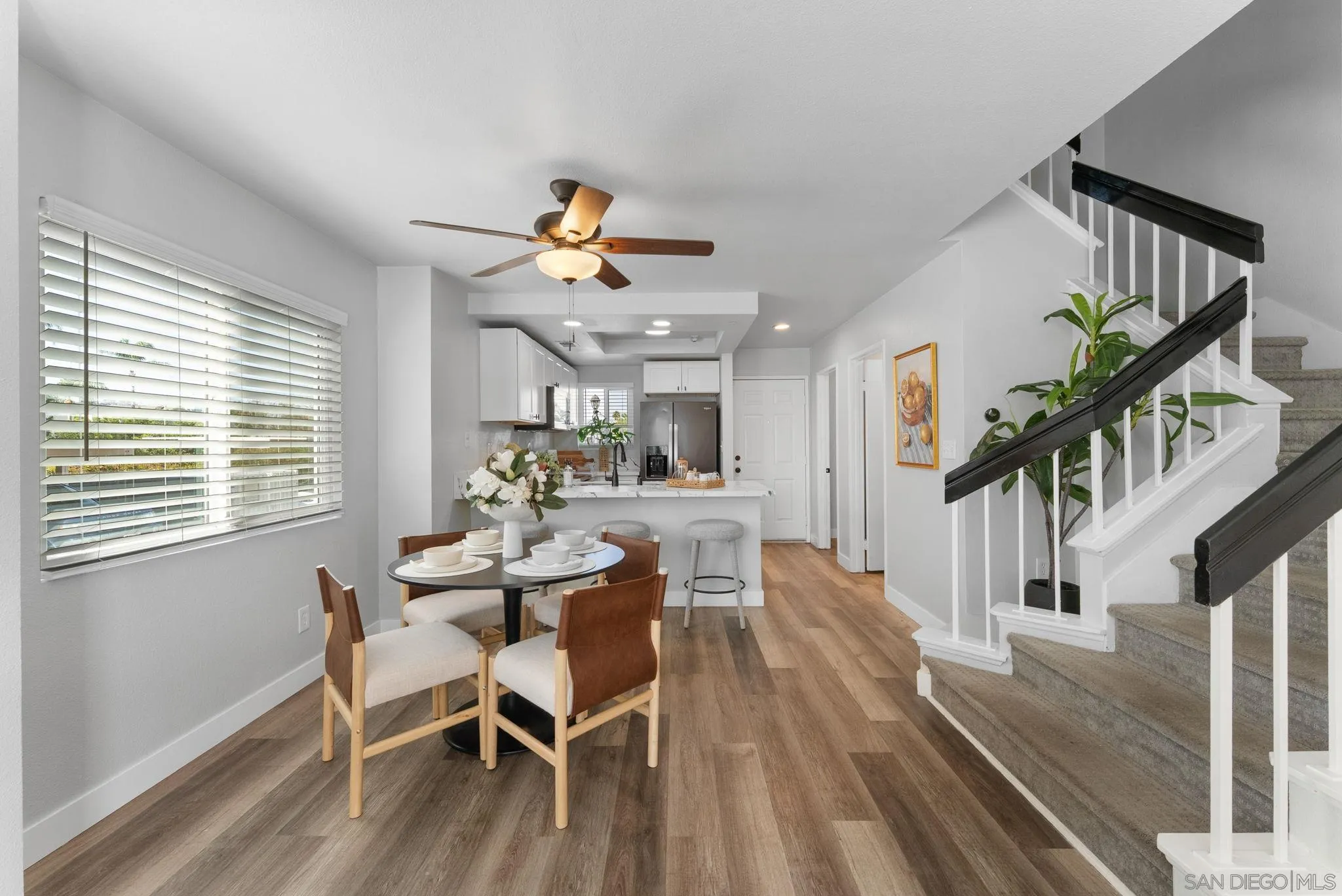 Open kitchen and dining area with a set table beside a carpeted staircase with black railings.