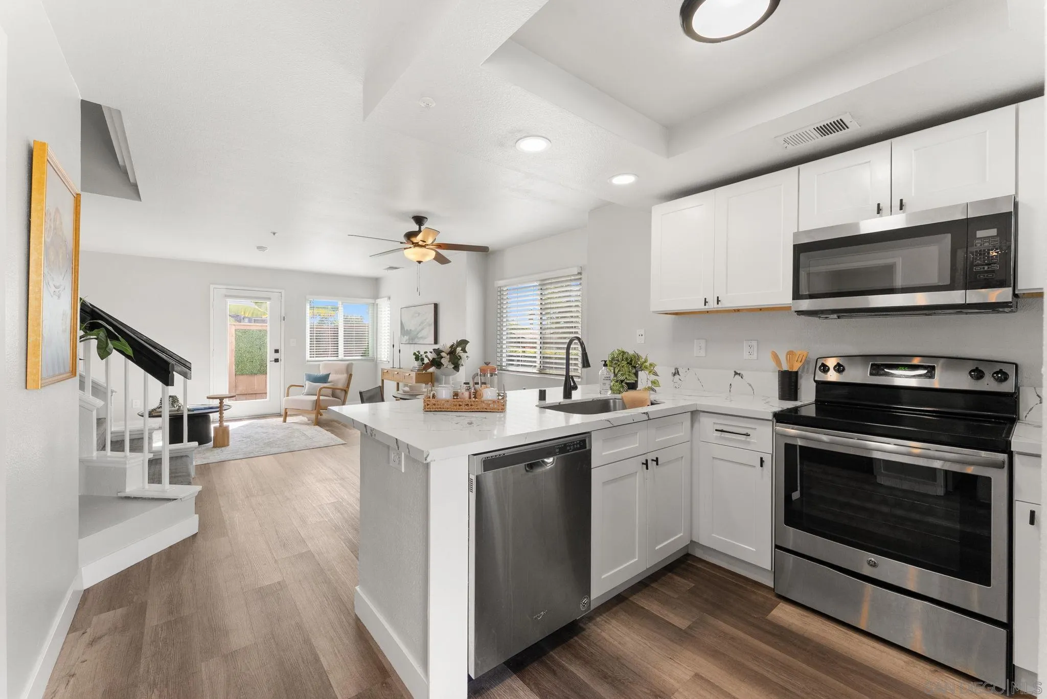 Open-plan kitchen with white cabinets, stainless steel appliances, and a marble-look island overlooking a sitting area.