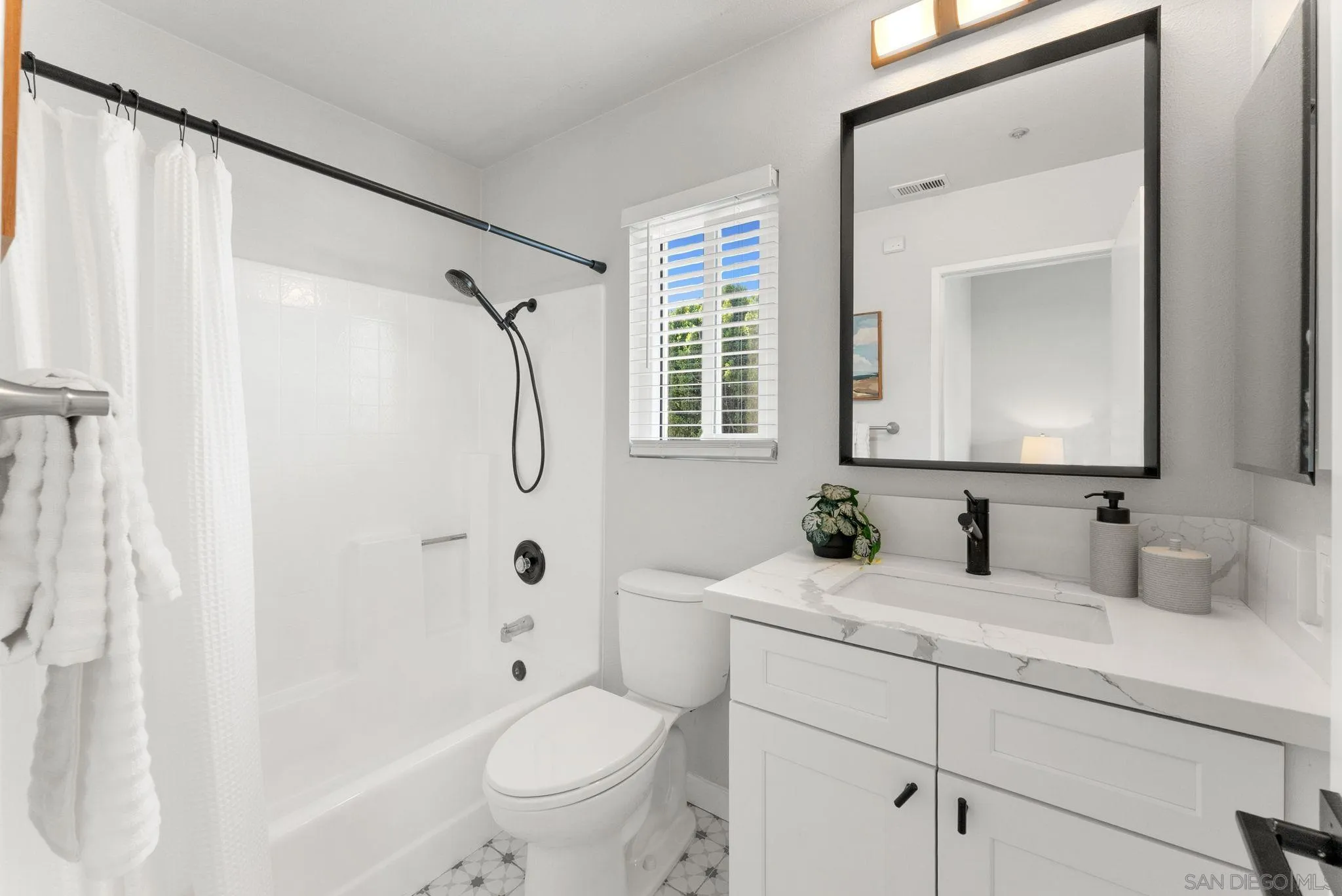 Bright bathroom with a white tub, black fixtures, marble-look vanity, and patterned floor tile.