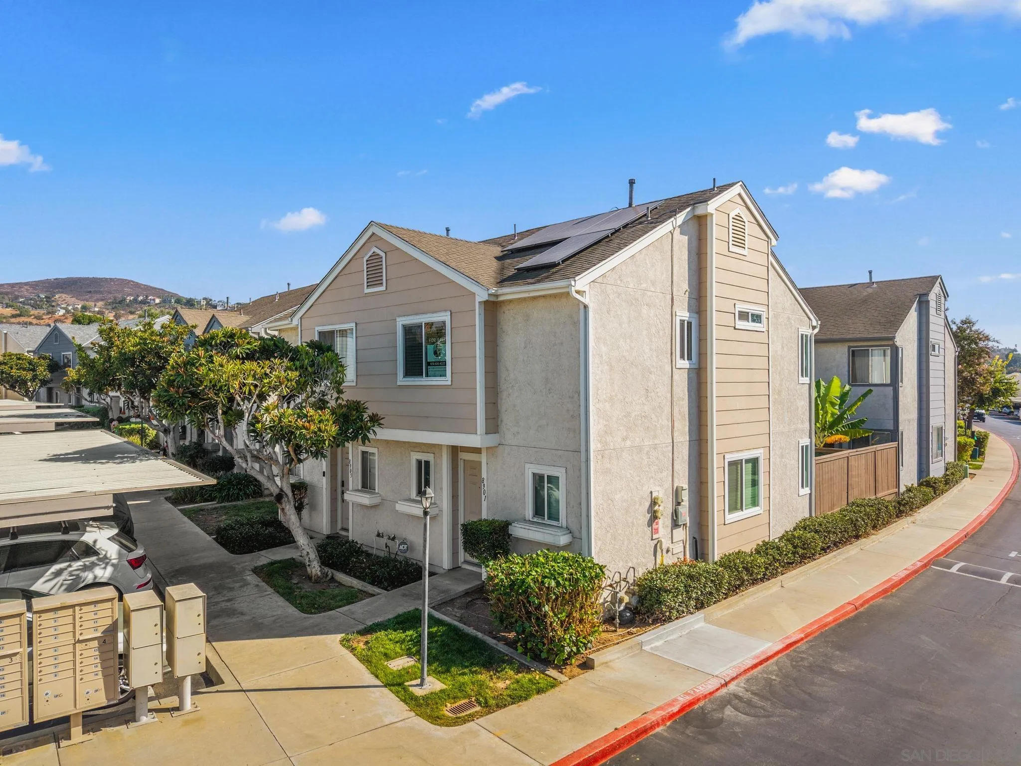 Beige two-story townhouse with rooftop solar panels, landscaped entry, and community mailboxes.