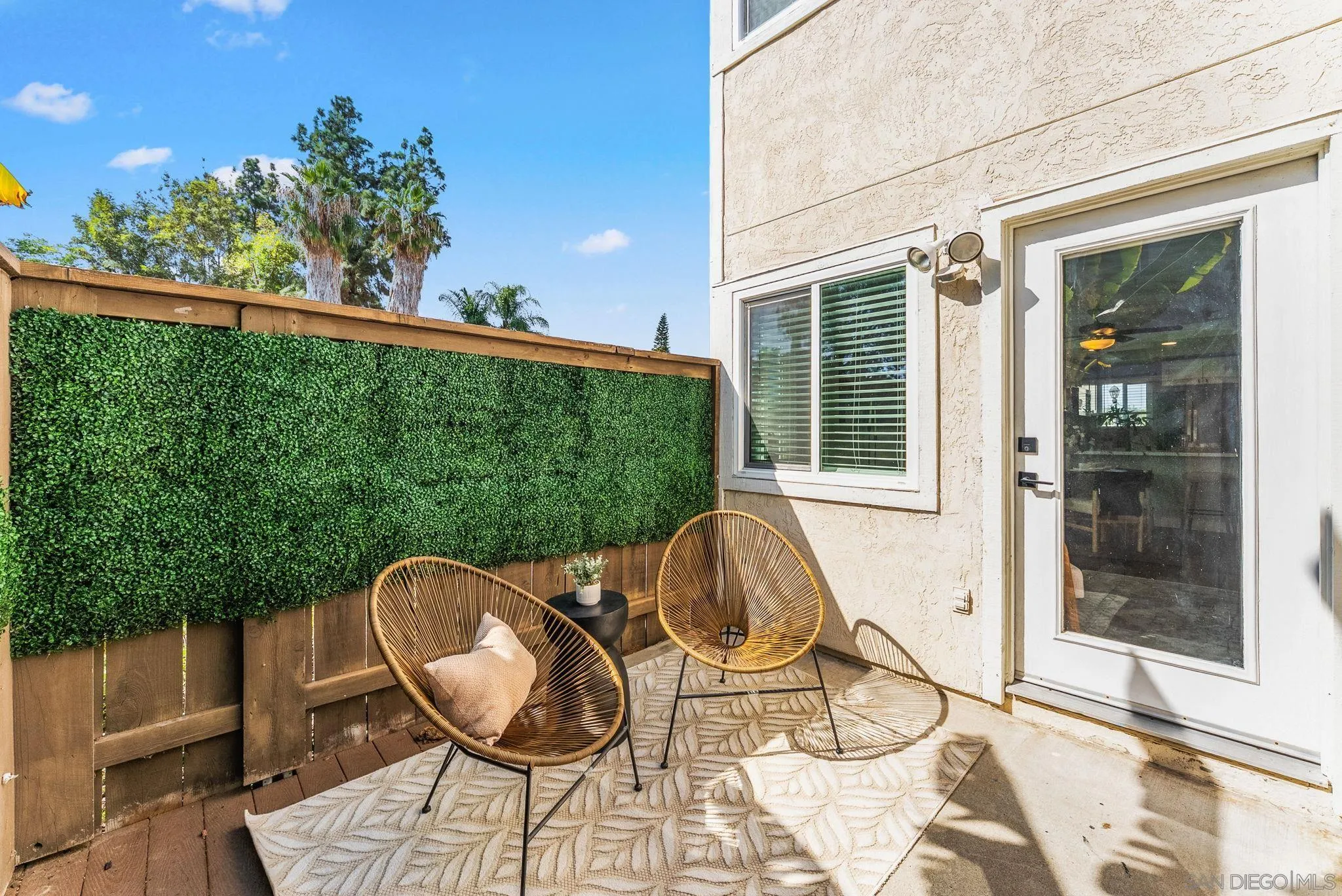 Outdoor patio with two woven chairs, a patterned rug, and a greenery-covered privacy fence.