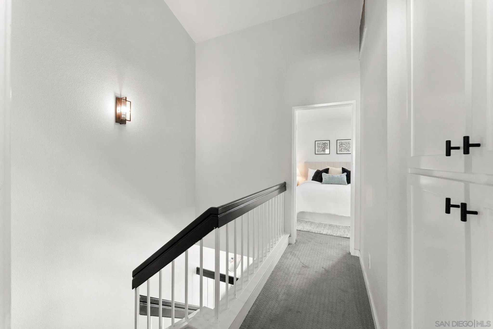 Upstairs hallway with a black-topped stair railing and a furnished bedroom visible through the doorway.