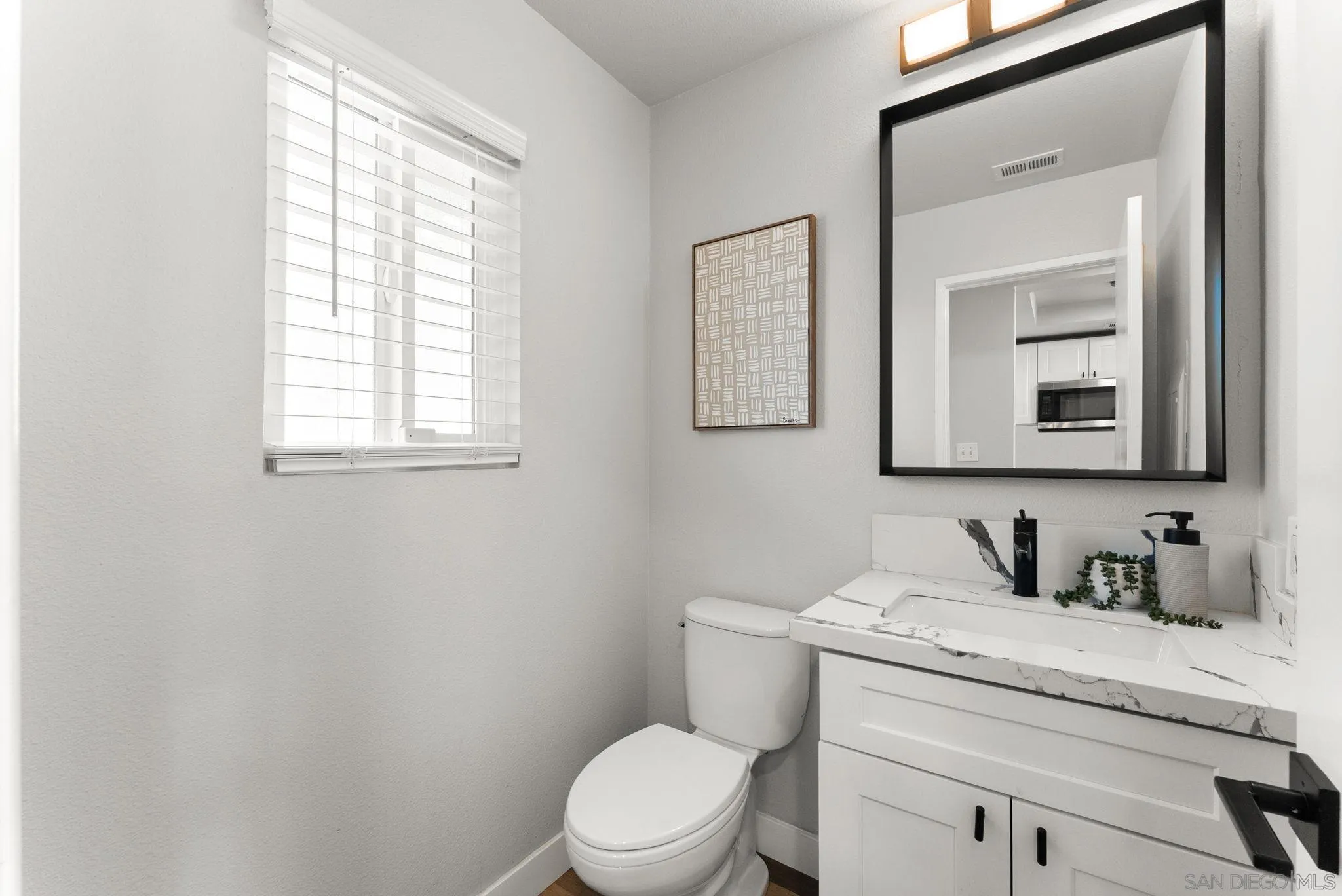 Bright bathroom with a marble-look vanity, black-framed mirror, and window with white blinds.