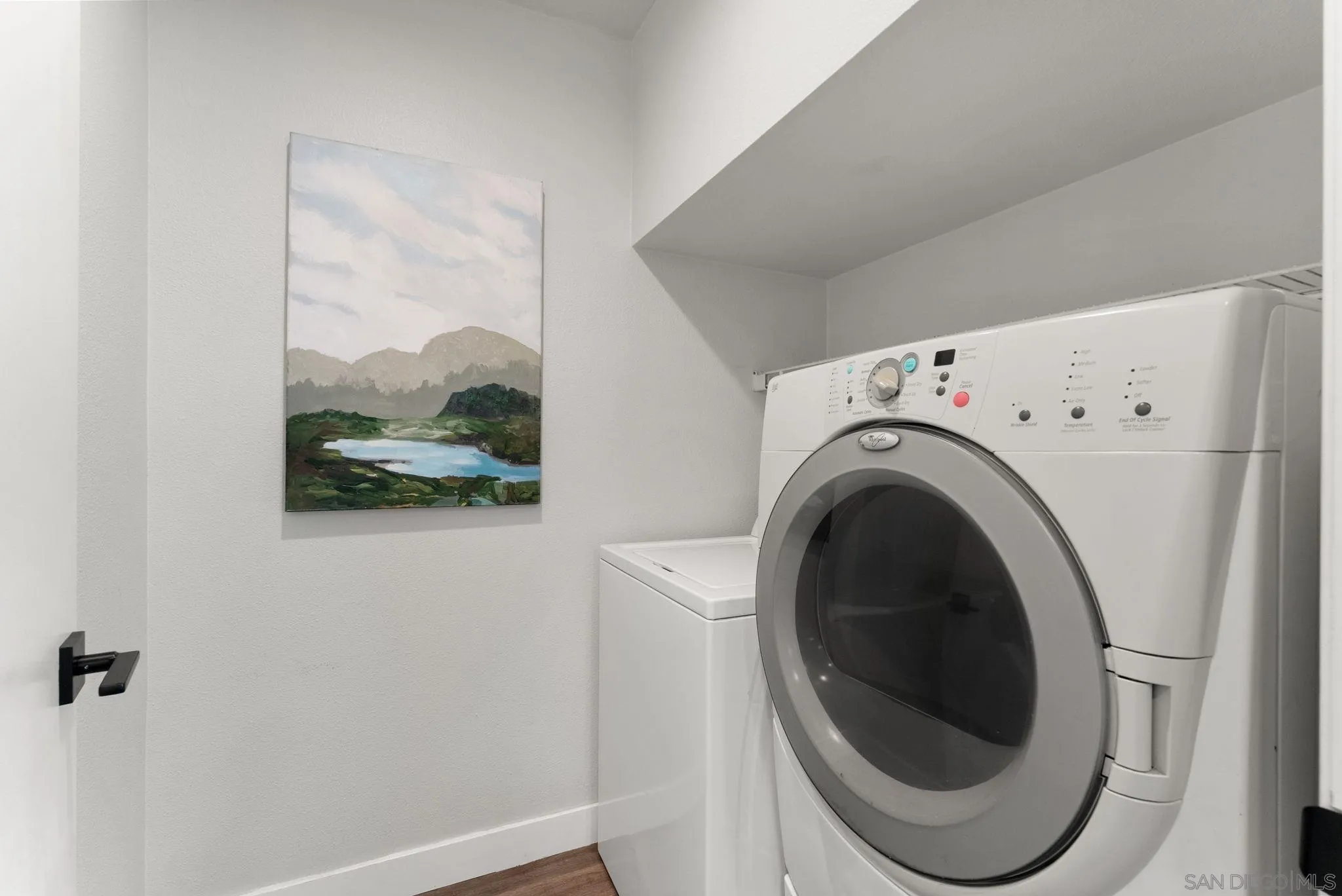 Laundry room with front-loading dryer, top-loading washer, and landscape painting.