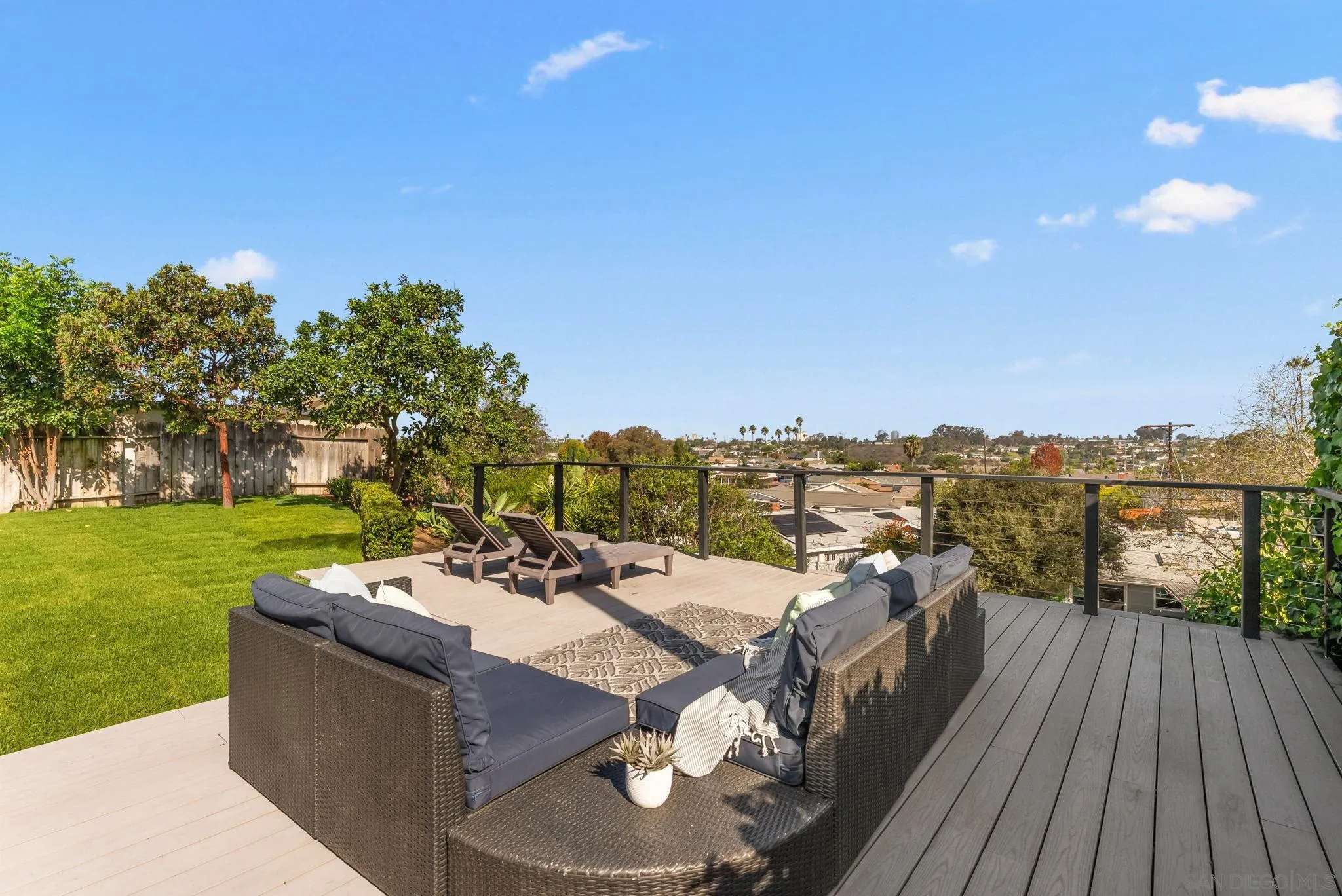 Furnished deck with wicker seating and lounge chairs overlooking a neighborhood.