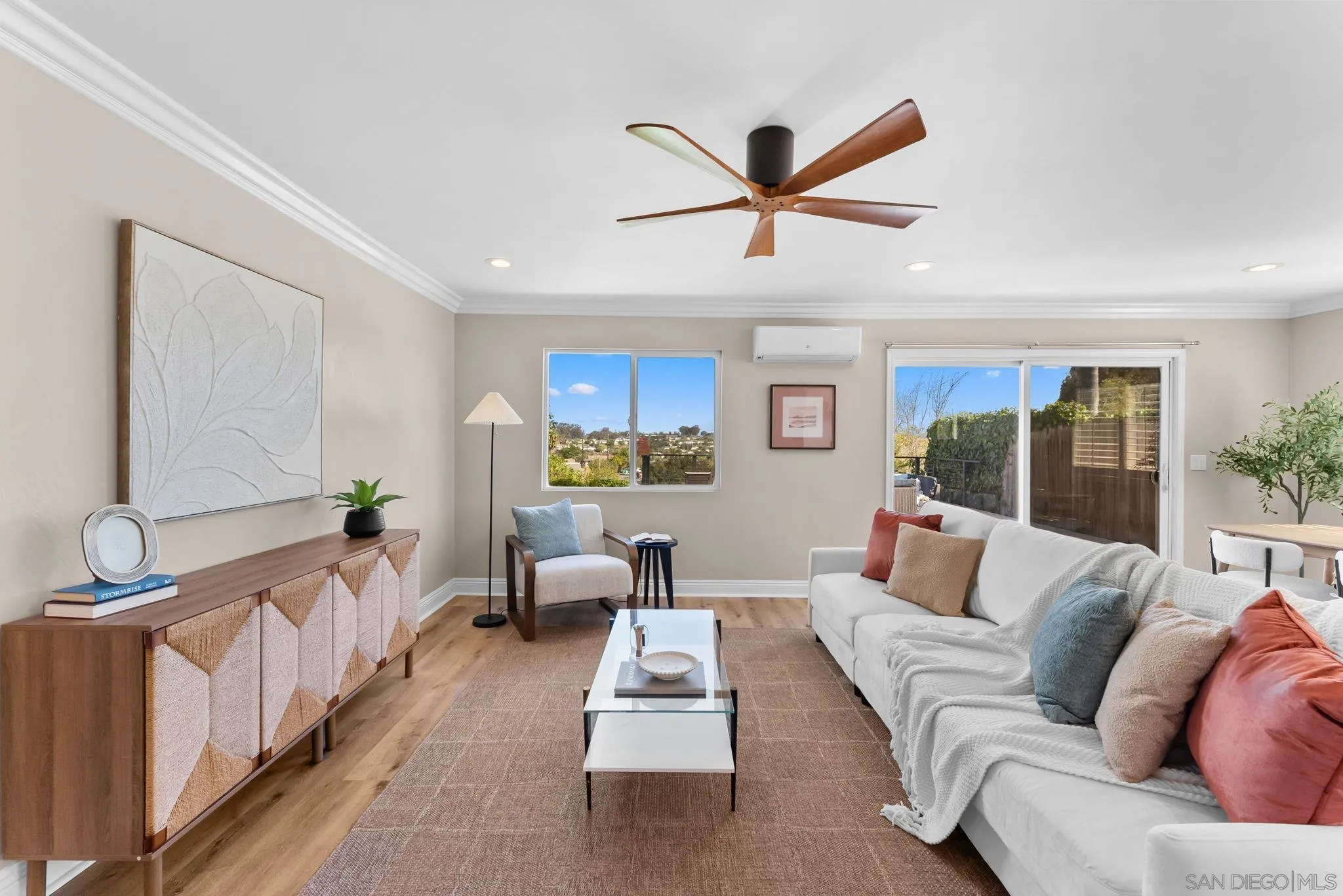 Furnished living room with a white sectional, wood cabinet, ceiling fan, and sliding doors to a patio.