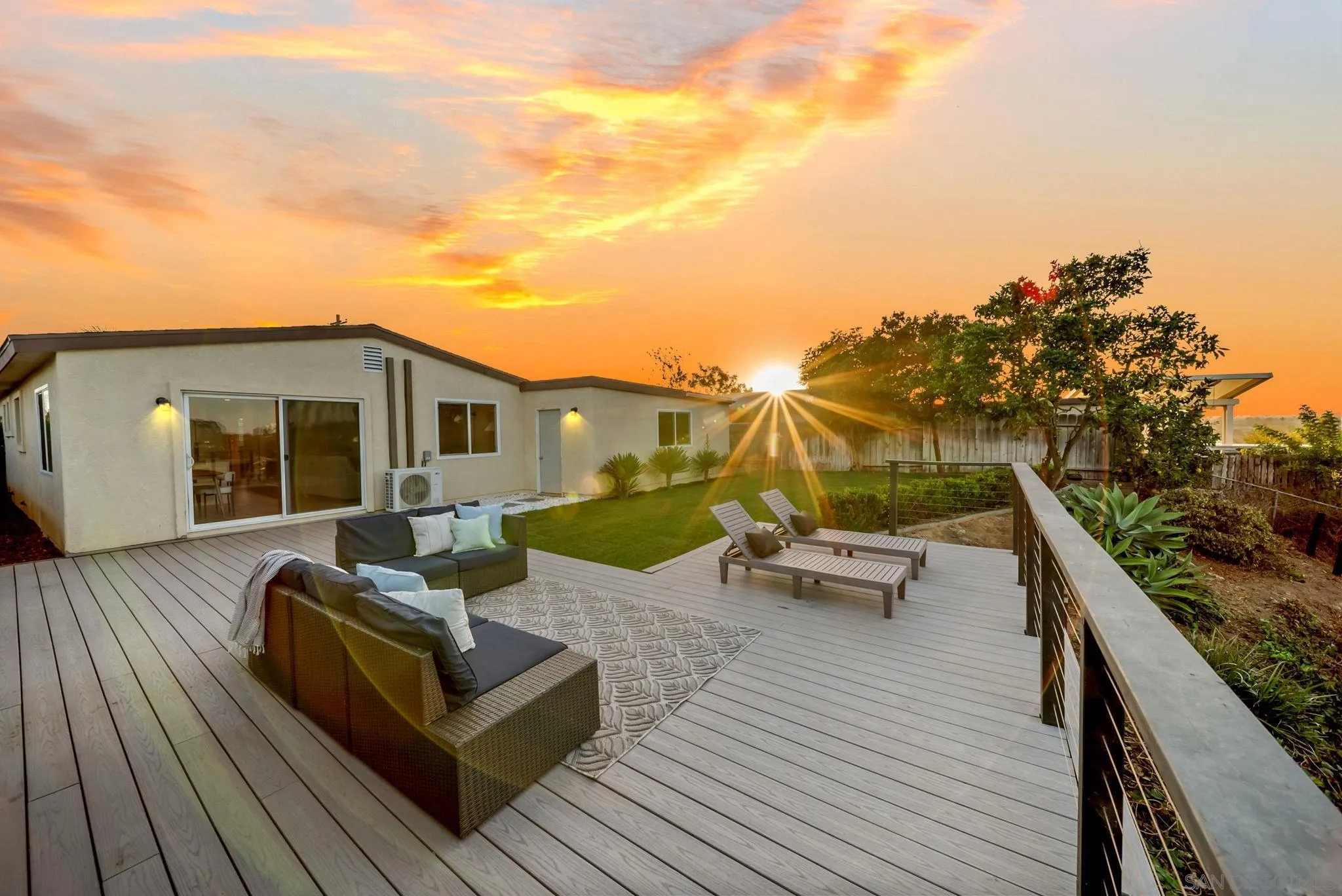 Backyard deck with lounge seating and chaise lounges beside a lawn at sunset.