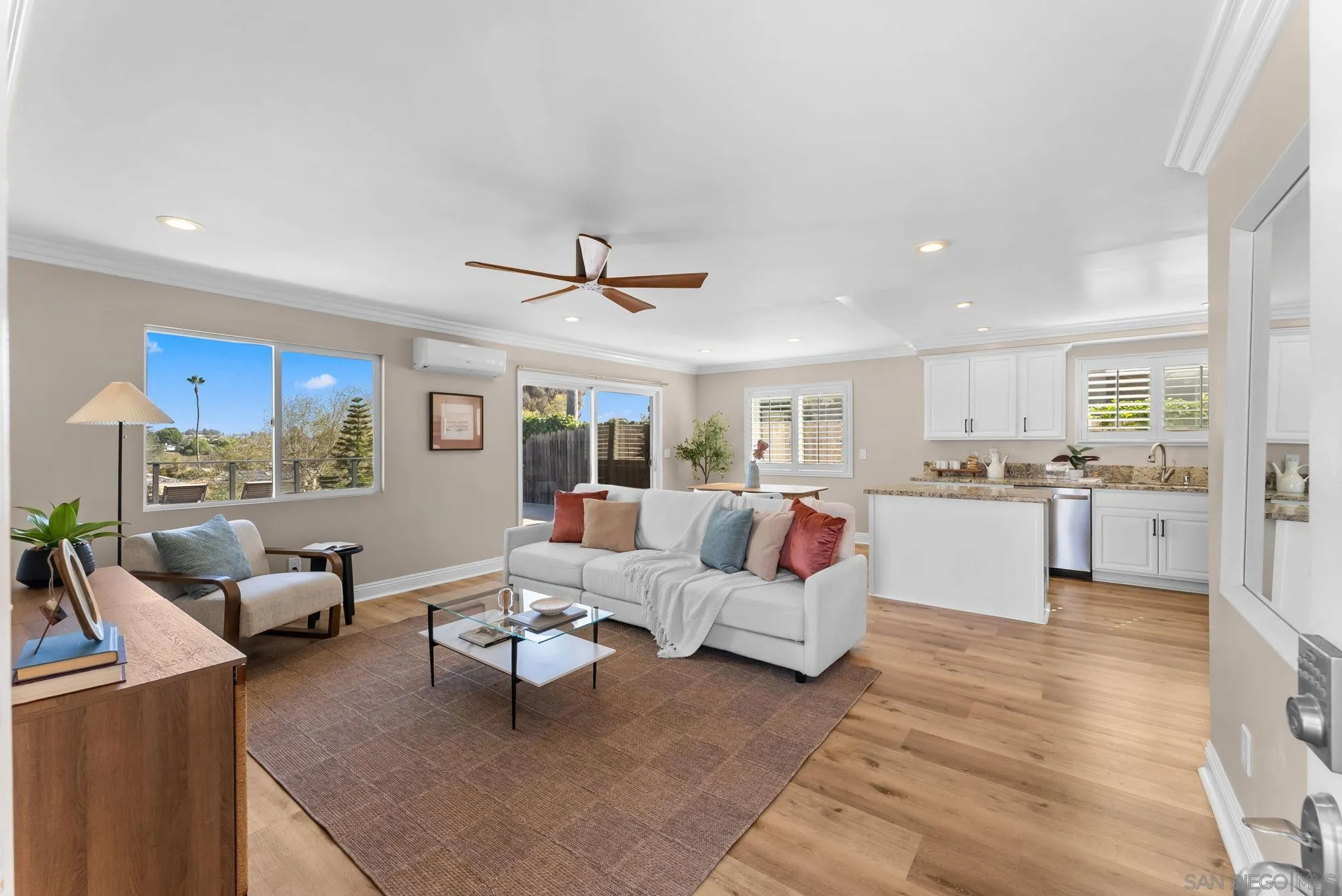 Open-plan living room and kitchen with a white sofa, wood floors, and large windows overlooking greenery.