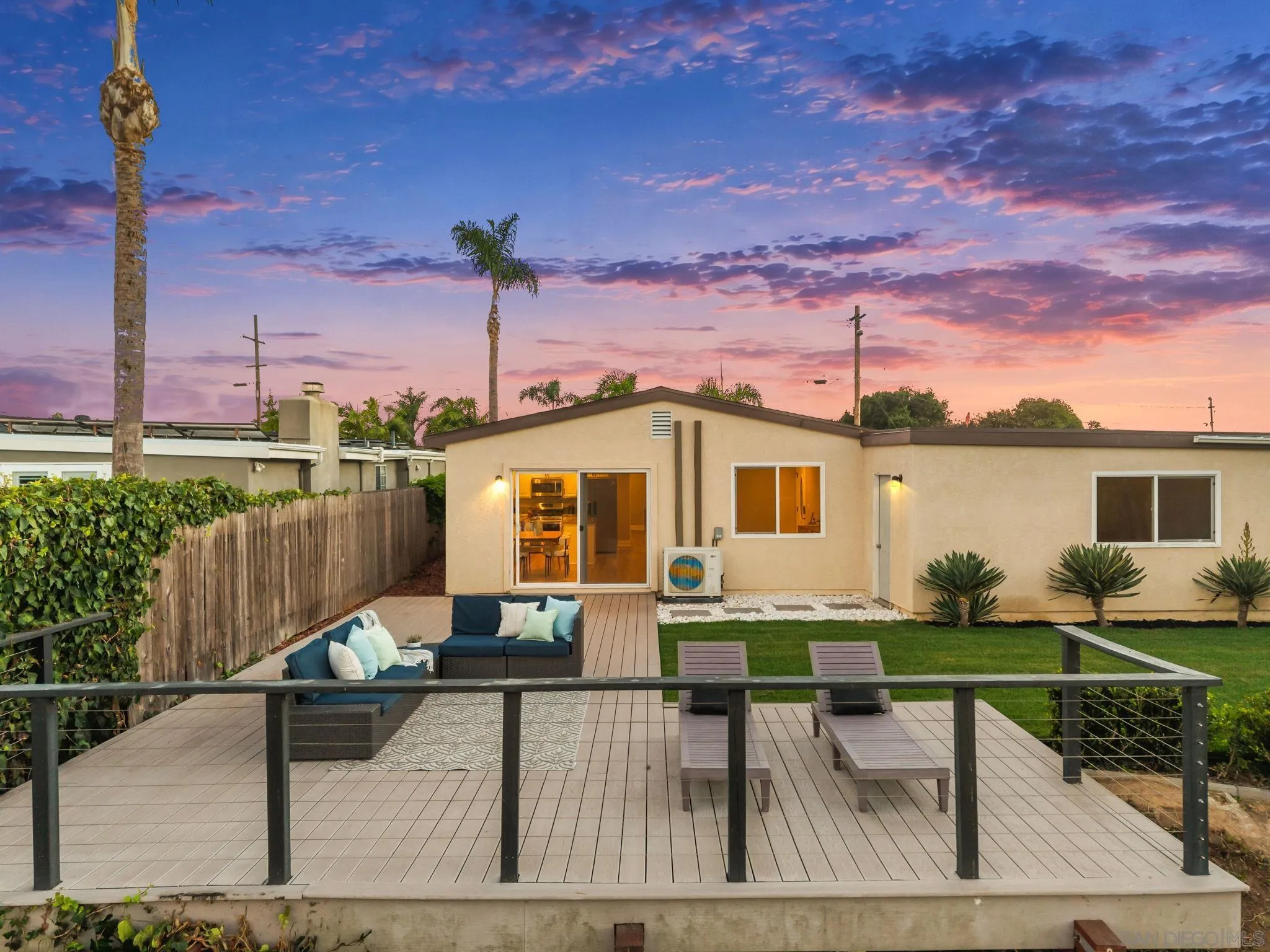 Single-story home with a furnished deck and lawn beneath a colorful dusk sky.