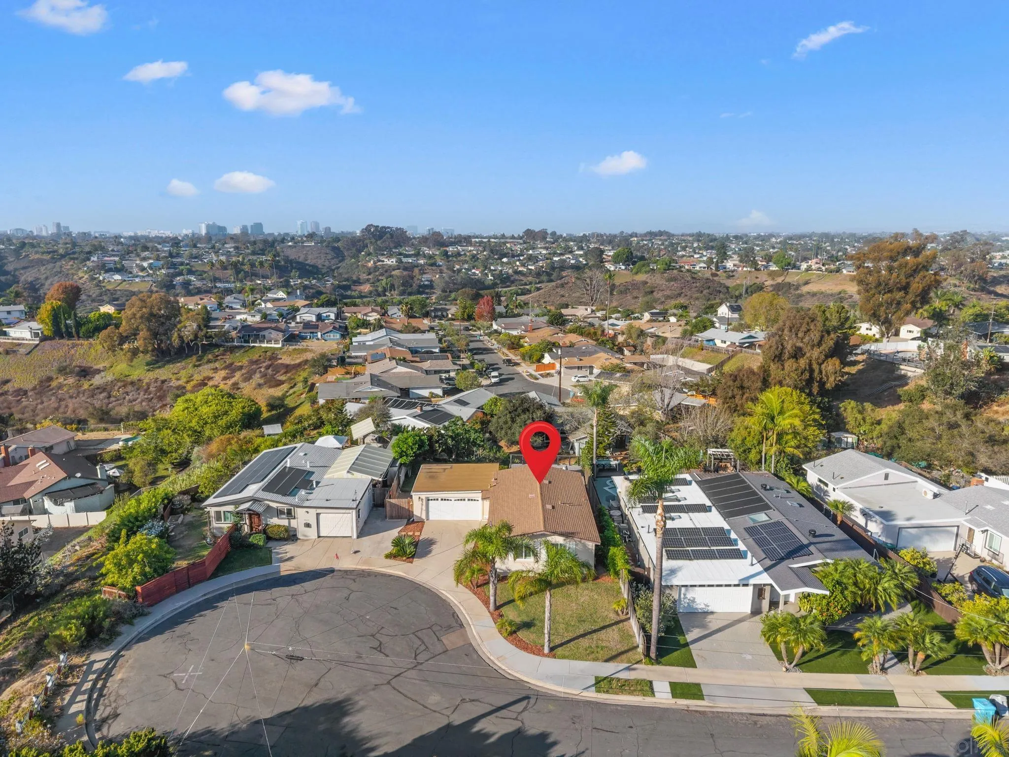 Aerial view of a cul-de-sac home marked by a red pin, with hillside homes and a distant skyline.