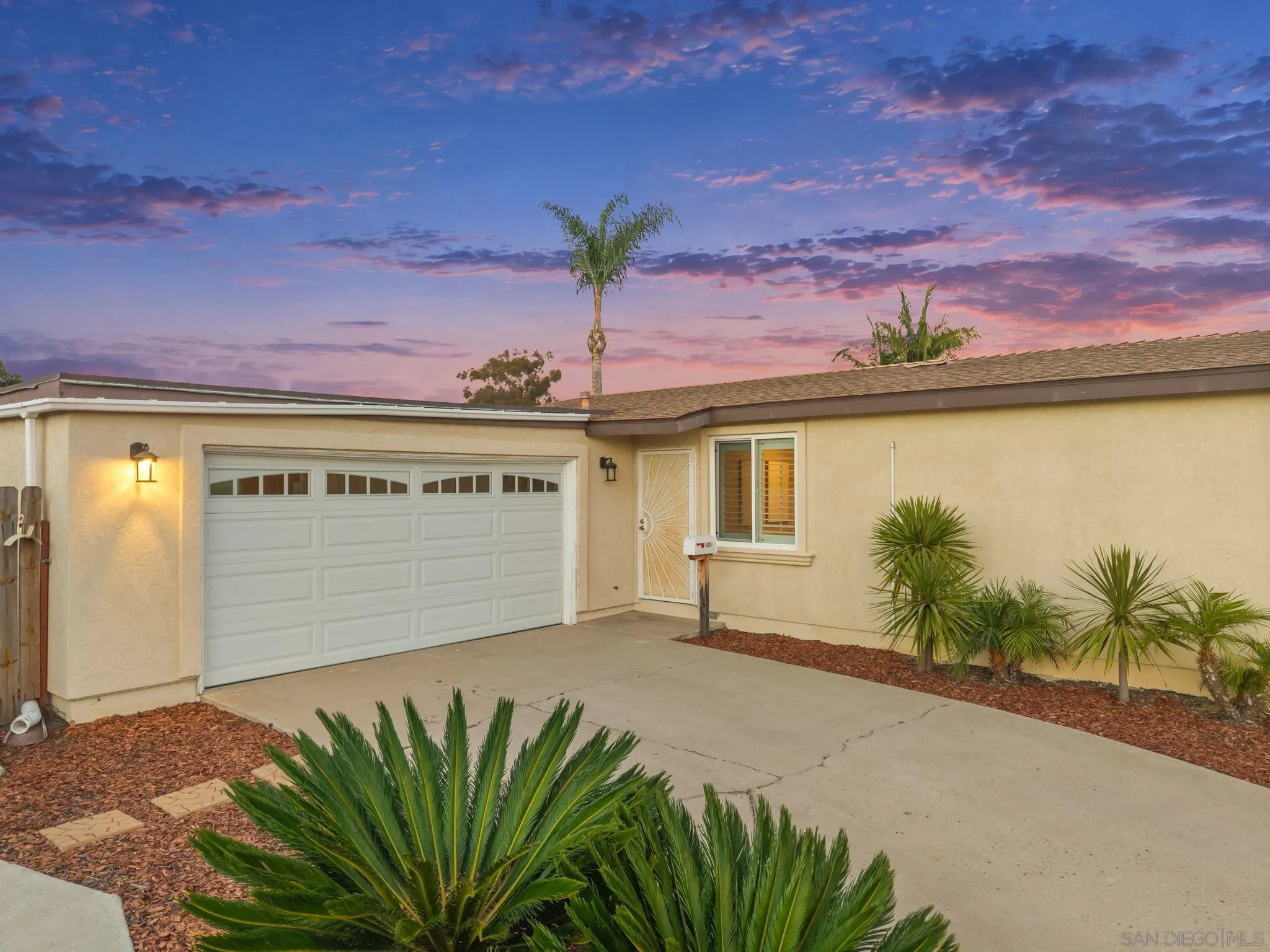 Single-story home with a two-car garage and landscaped driveway beneath a colorful dusk sky.