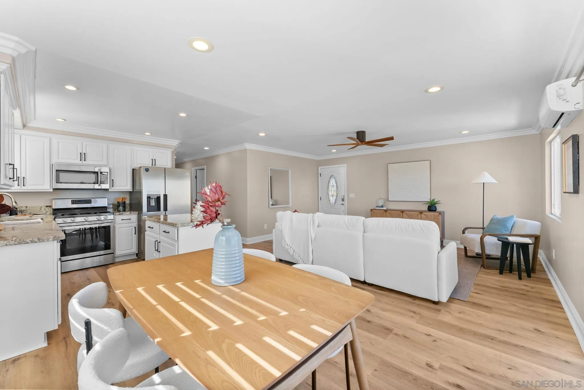 Open-plan kitchen and living room with white cabinetry, stainless appliances, and a wood dining table.