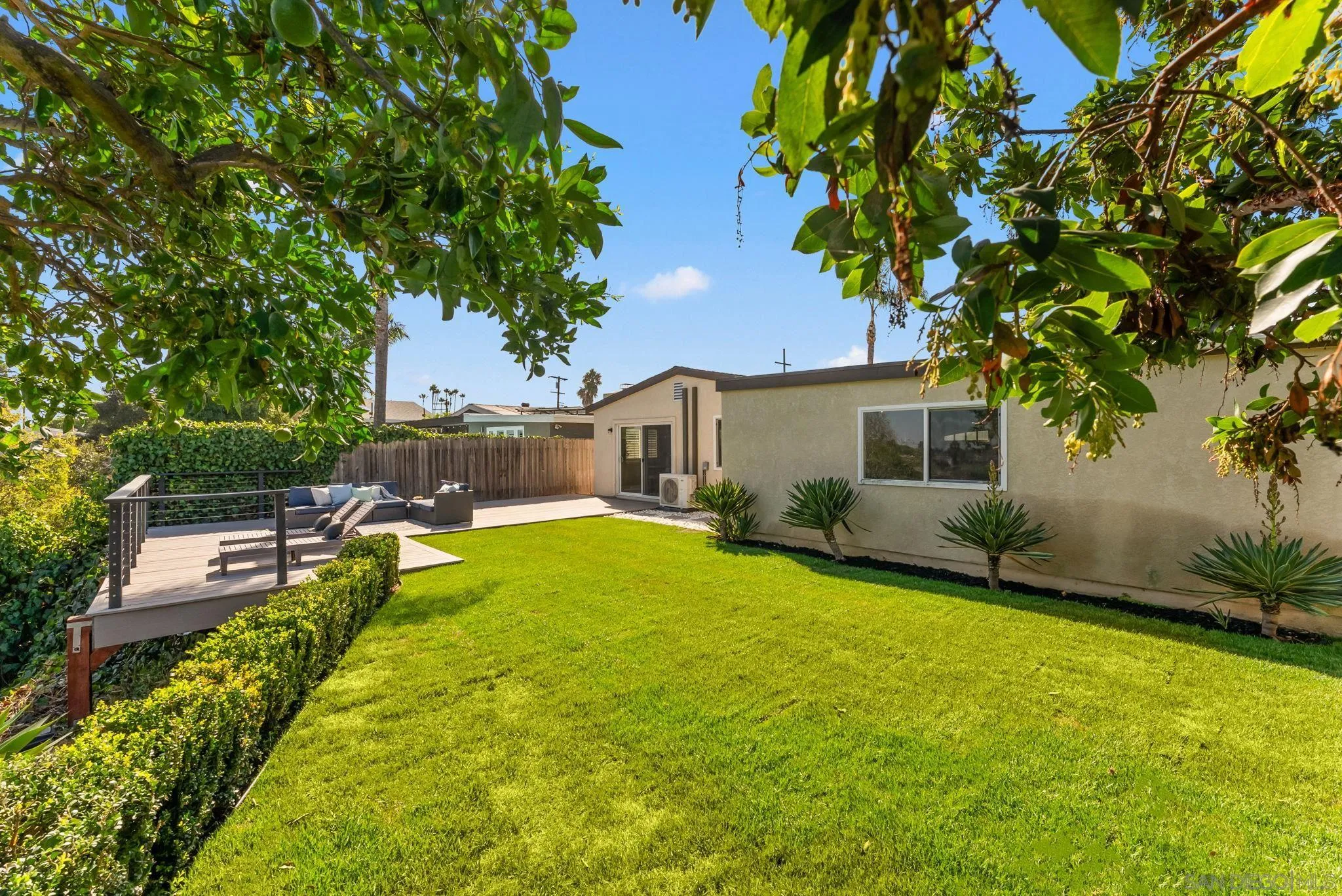 Backyard with a wide lawn and raised wood deck beneath mature trees.
