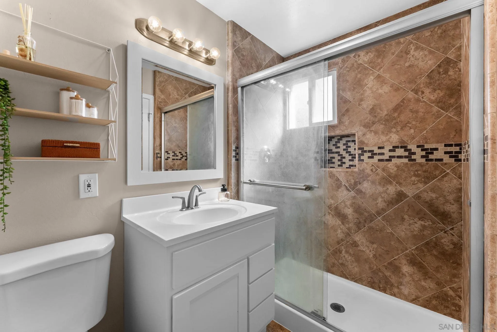 Bathroom with a white vanity and glass-enclosed shower lined in brown tile.