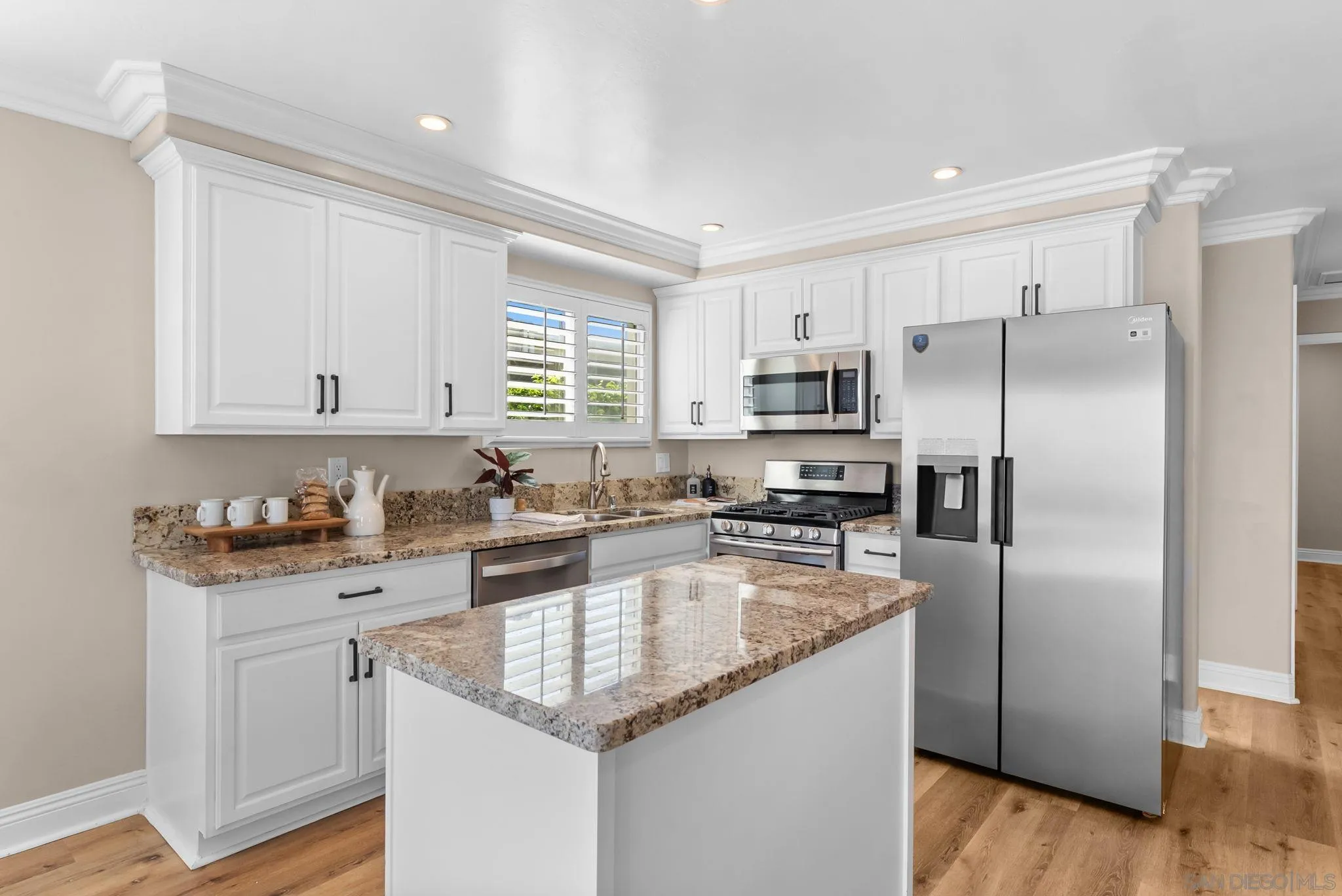 Kitchen with white cabinets, granite island, stainless steel appliances, and plantation shutters.