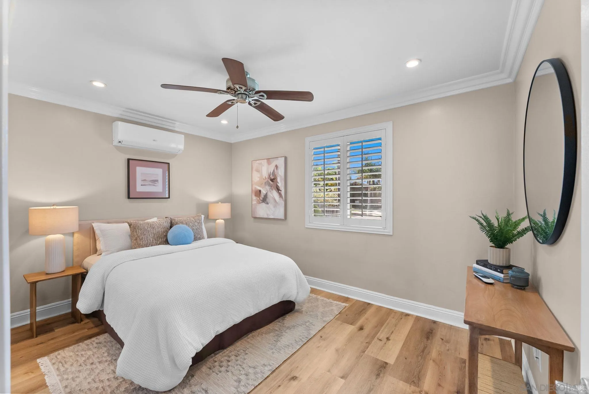 Bedroom with a white-covered bed, plantation shutters, wood furnishings, and a ceiling fan.