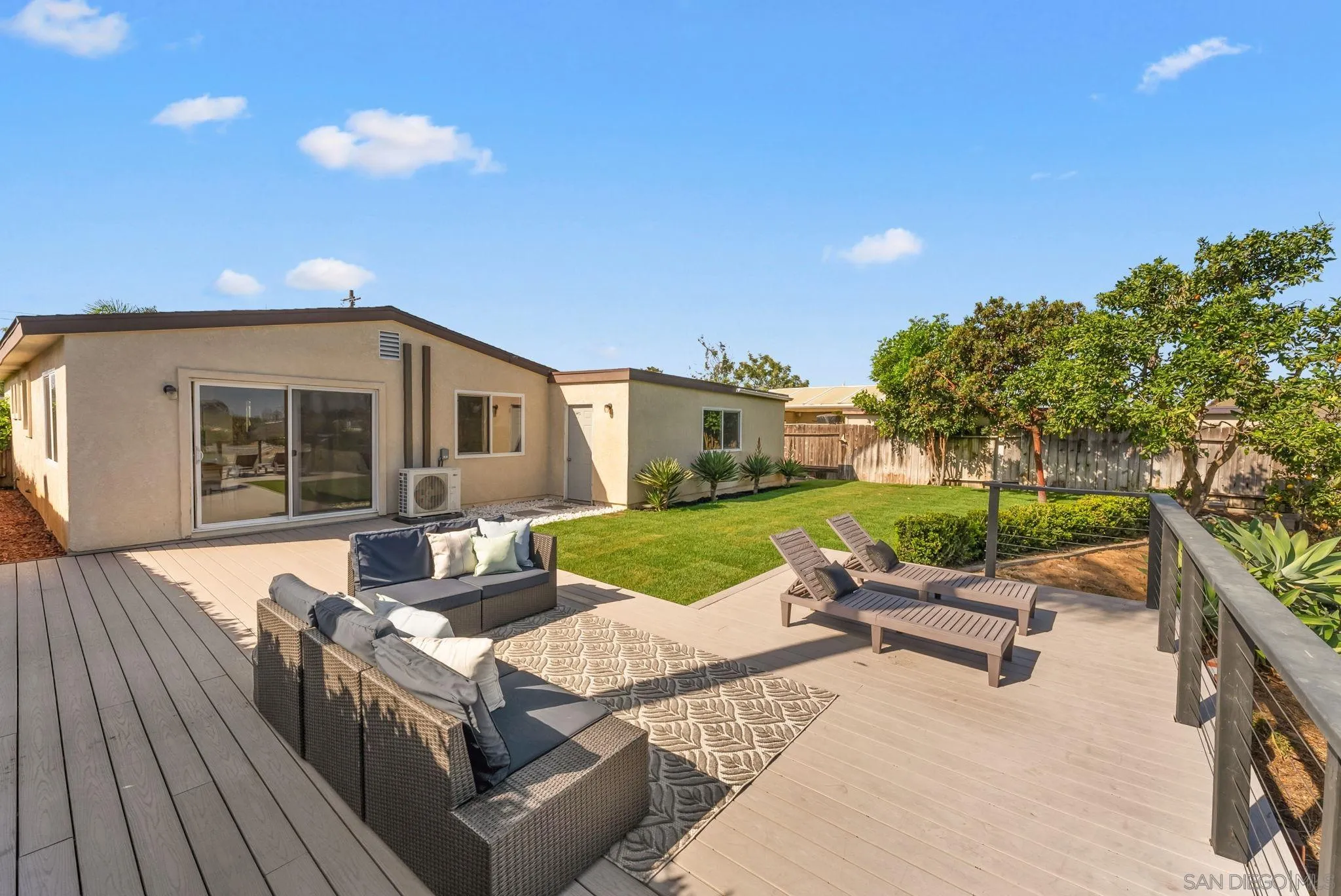 Backyard deck with outdoor lounge seating beside a green lawn and mature trees.