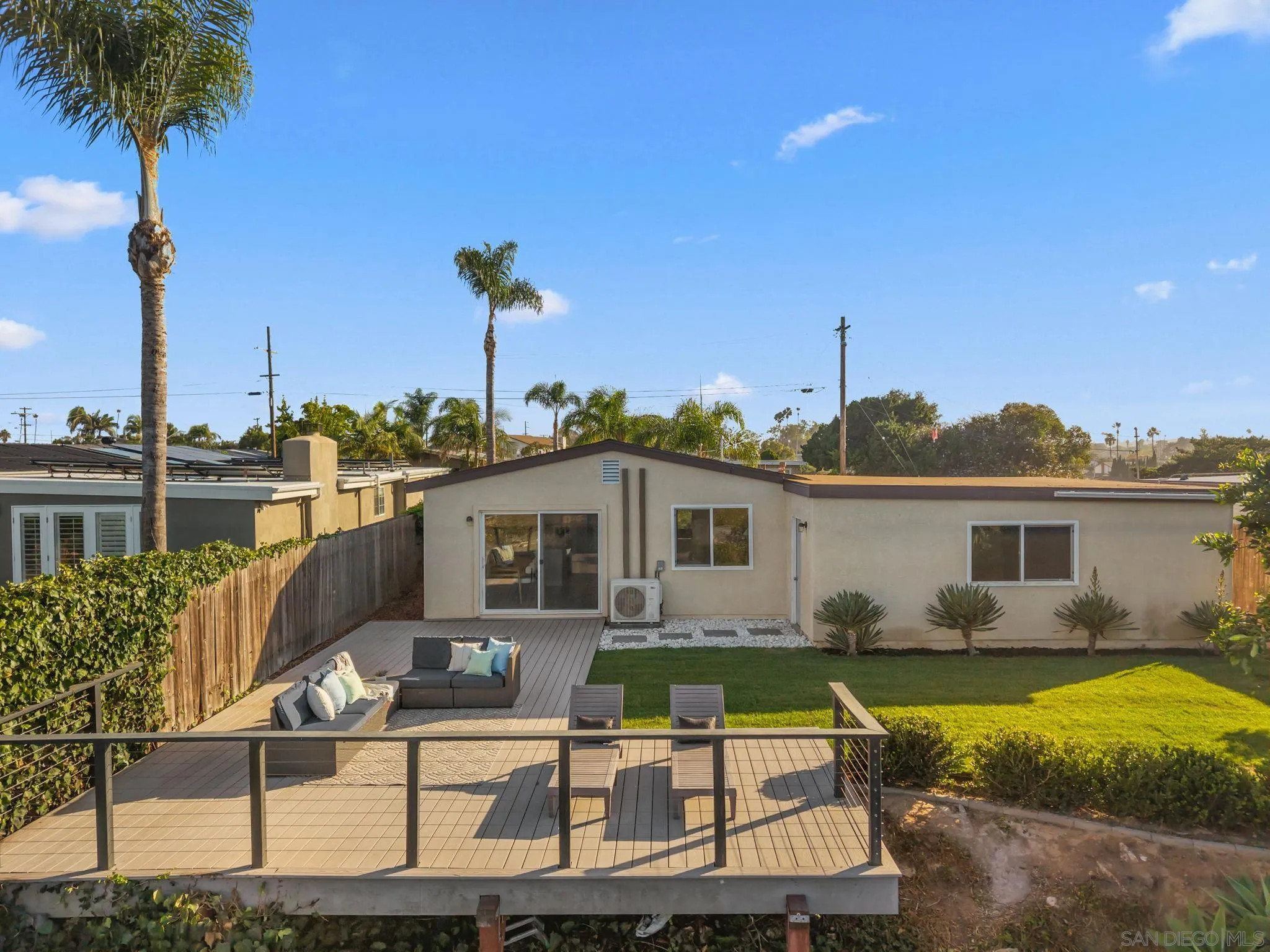Home’s backyard with a furnished raised deck, lawn, and palm trees.