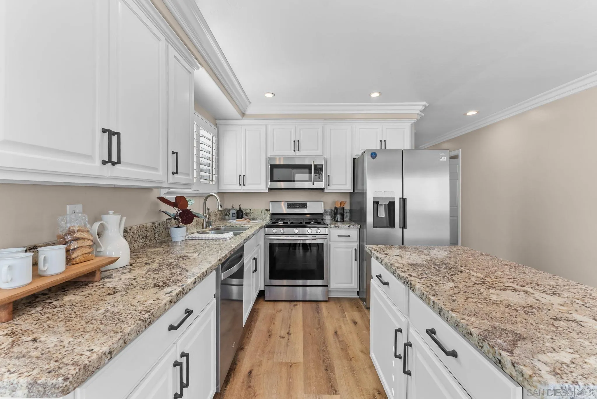 Kitchen with white shaker cabinets, granite counters, stainless steel appliances, and warm wood flooring.